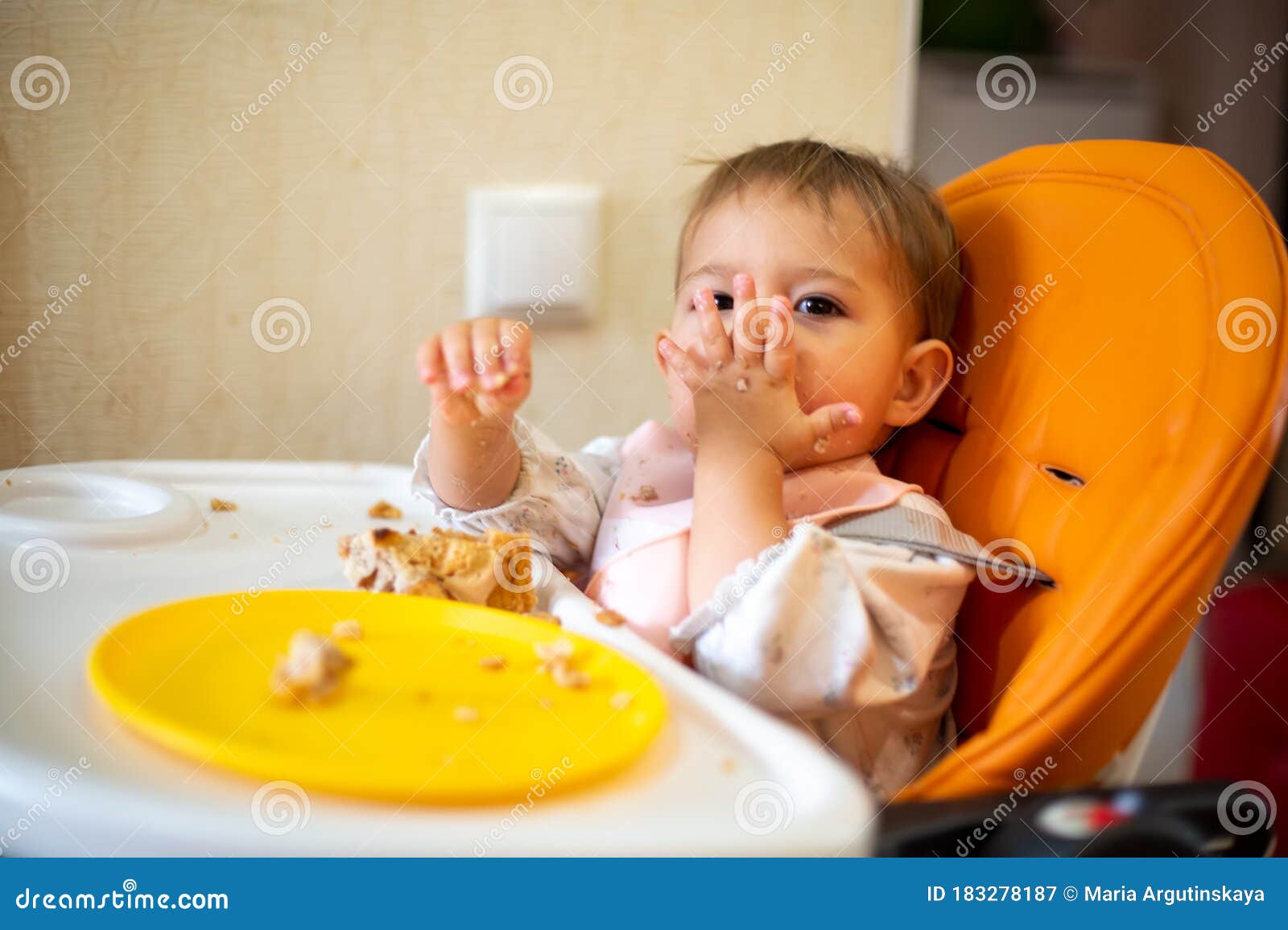 Cute Baby Sits In An Orange Baby Chair With A Table With ...