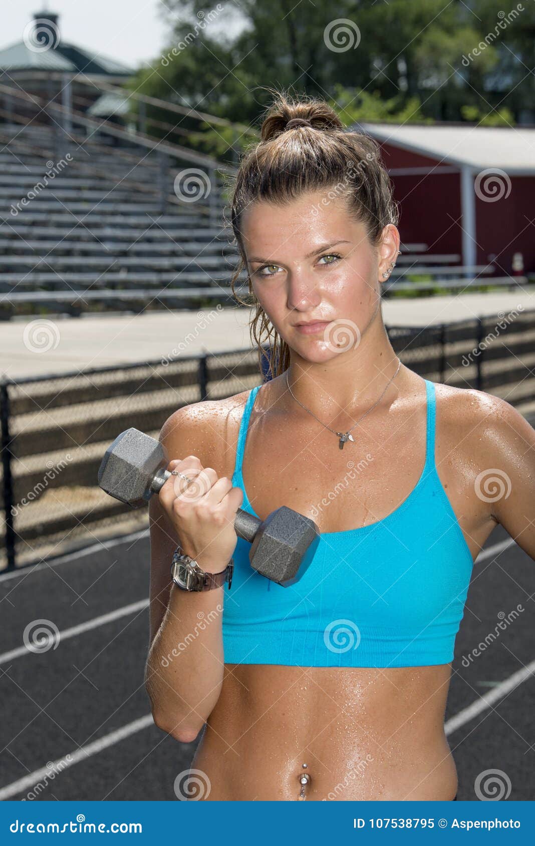Cute and fit young teen Caucasian girl working out on outdoor track  glistens with sweat in blue sports bra Stock Photo