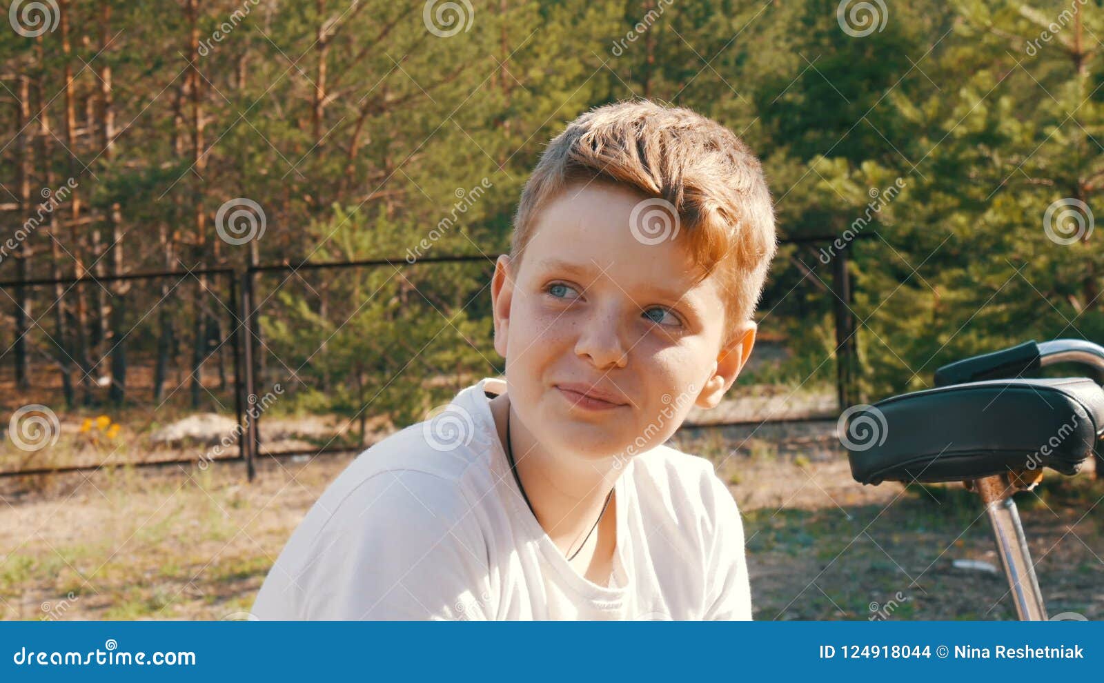 Cute Blonde With Blue Eyes A Teenager Boy Sits And Smile In A Park