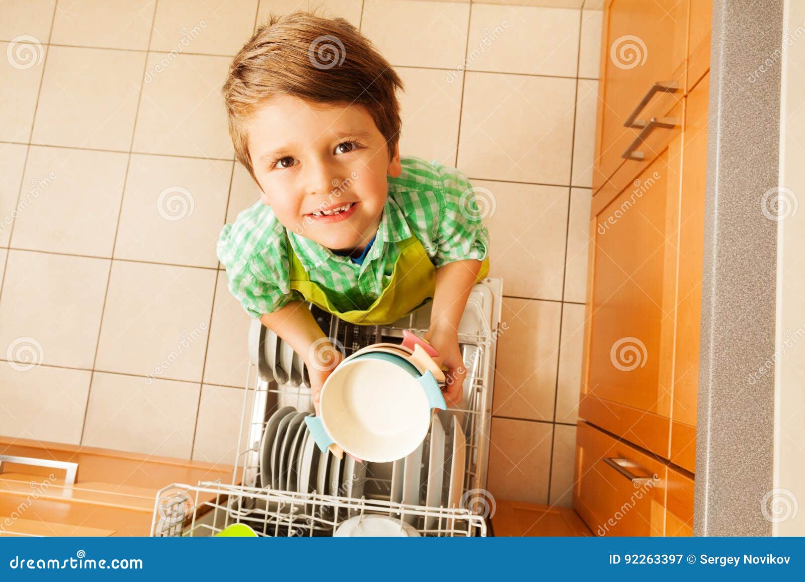 cute boy holding bowls standing next to dishwasher