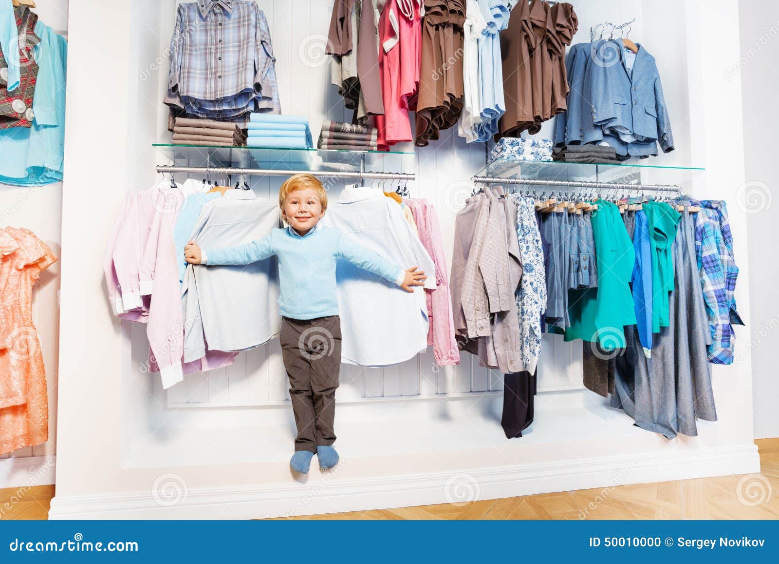 Cute Boy Stands among Clothes on Hangers and Shelf Stock Photo - Image ...