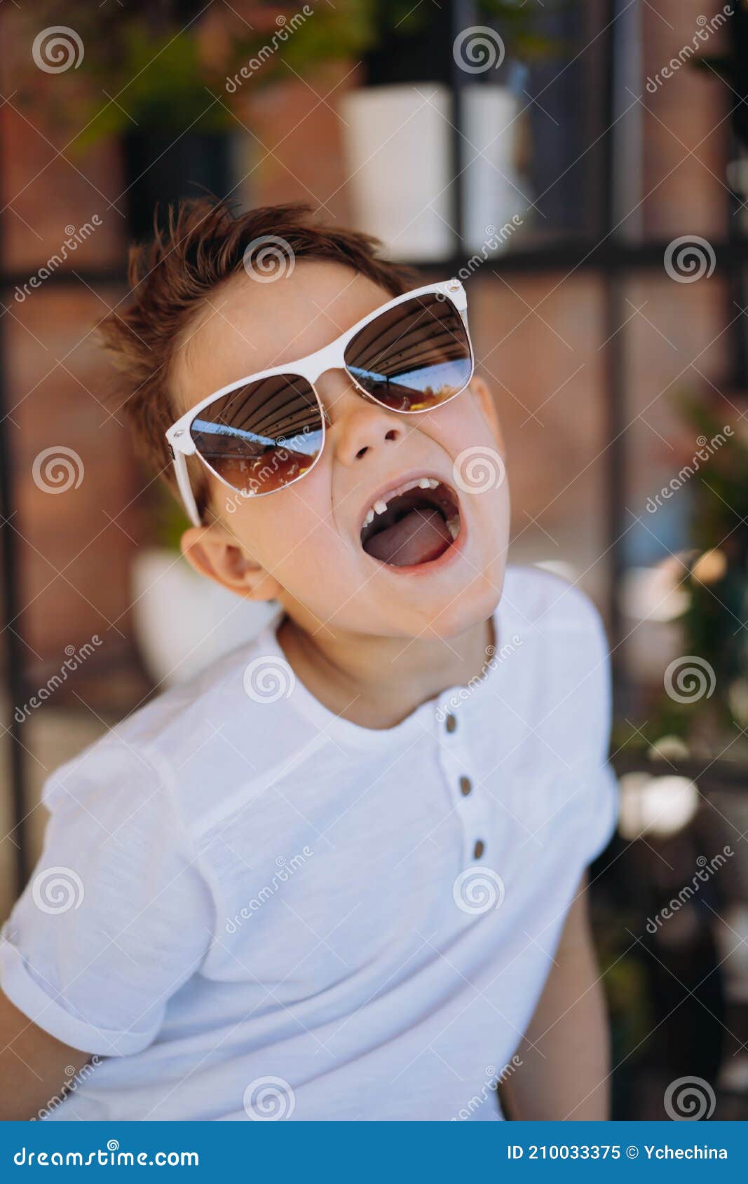 cute cauasian boy in white tee shirt and sunglasses posing for camera and showing his lost tooth.