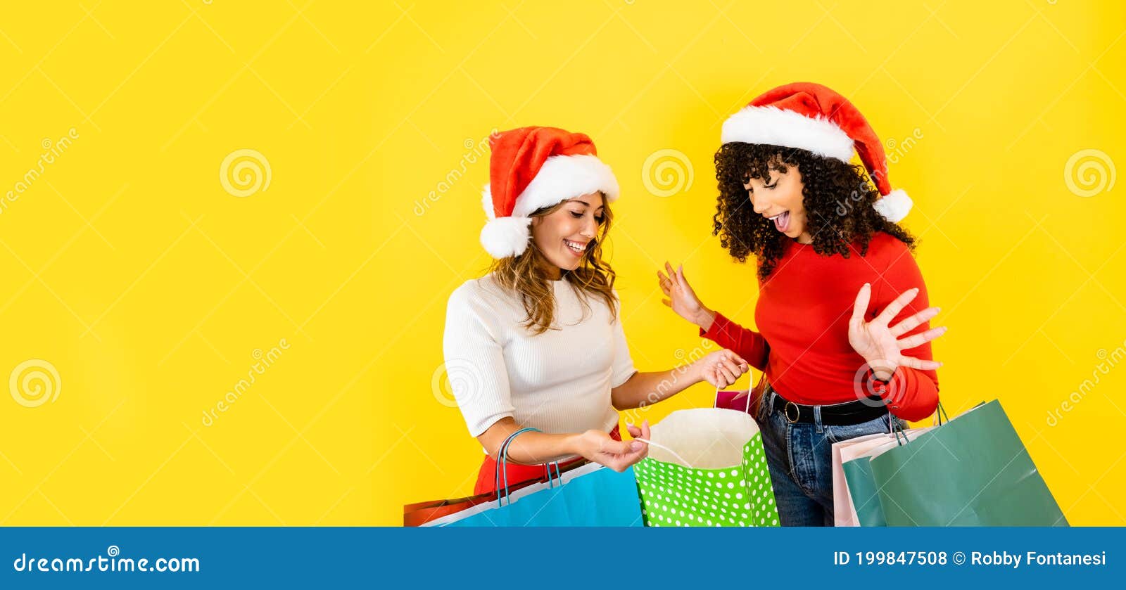 cute caucasian blonde young woman open her shopping bag showing to her black hispanic female friend - two millennial multiracial