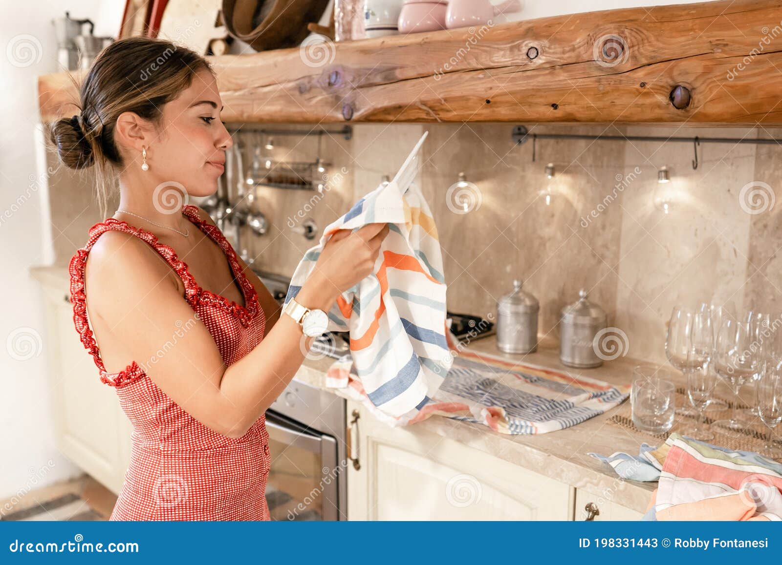 cute caucasian young woman drying dishes with a rag at home after a party in a rustic kitchen - female roles and housework in