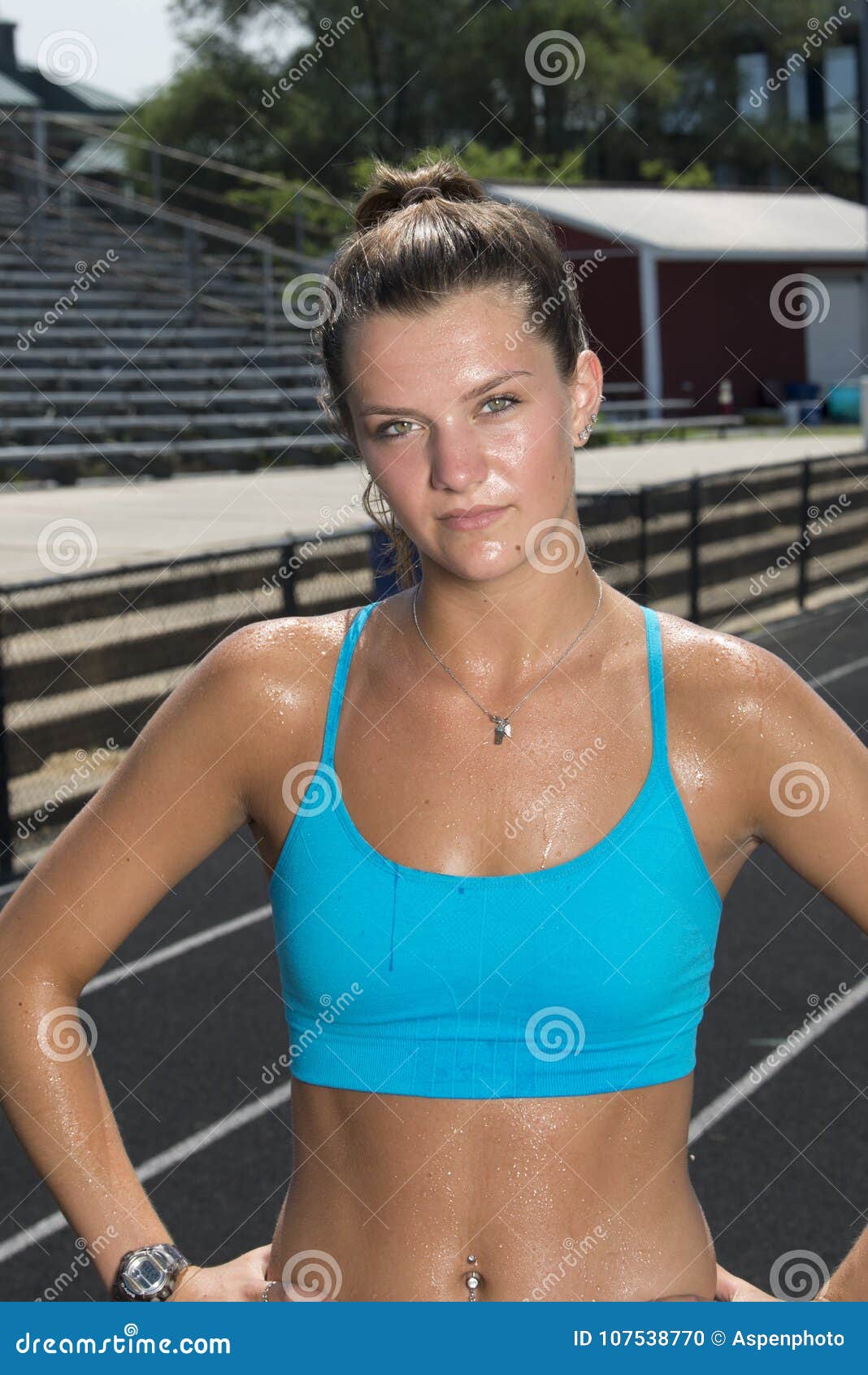 Cute and fit young teen Caucasian girl working out on outdoor track  glistens with sweat in blue sports bra as she pours water on her face Stock  Photo
