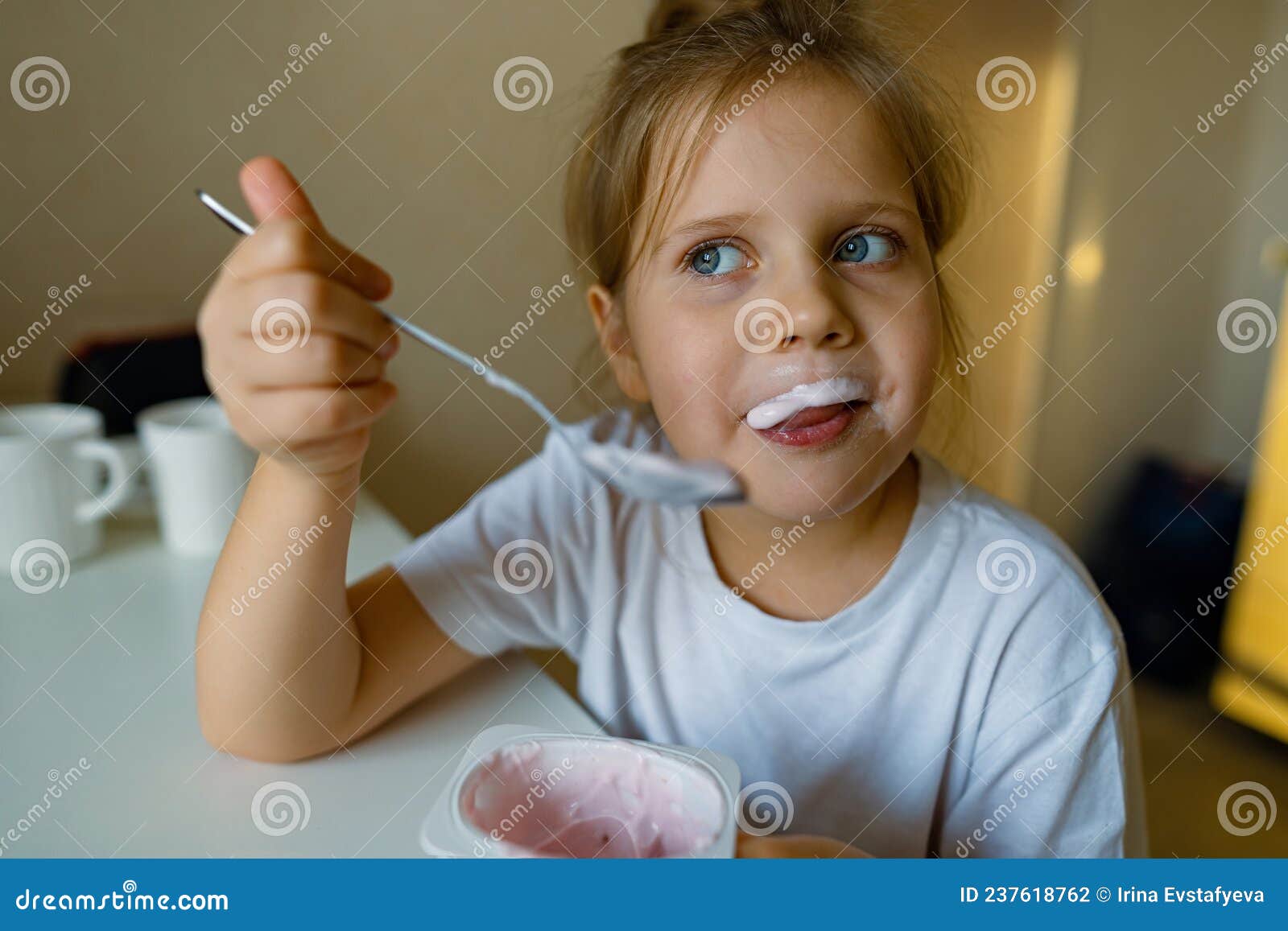 cute girl eats yogur with appetite, has dirty mouth, has fun, grimaces