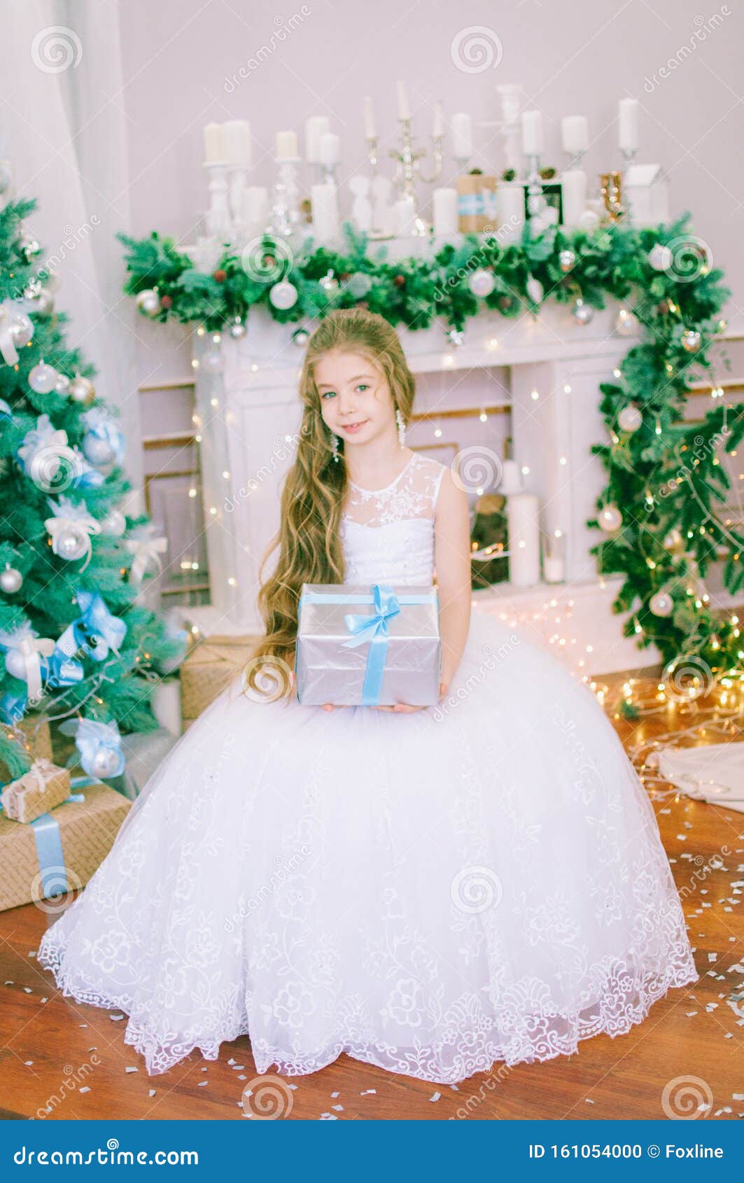 Cute Girl With Long Hair In A White Ball Gown By The Christmas Tree In Holiday Dresses With