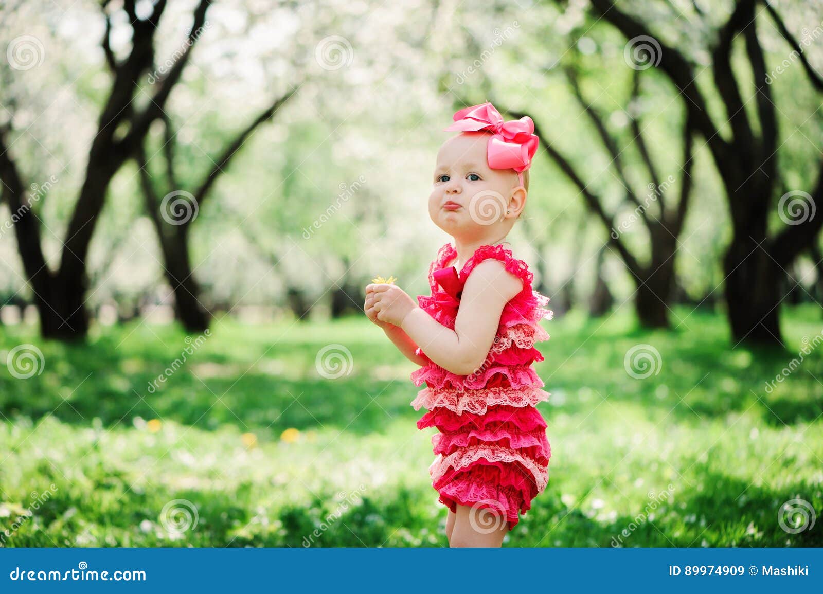 cute happy baby girl in funny pink romper walking outdoor in spring garden