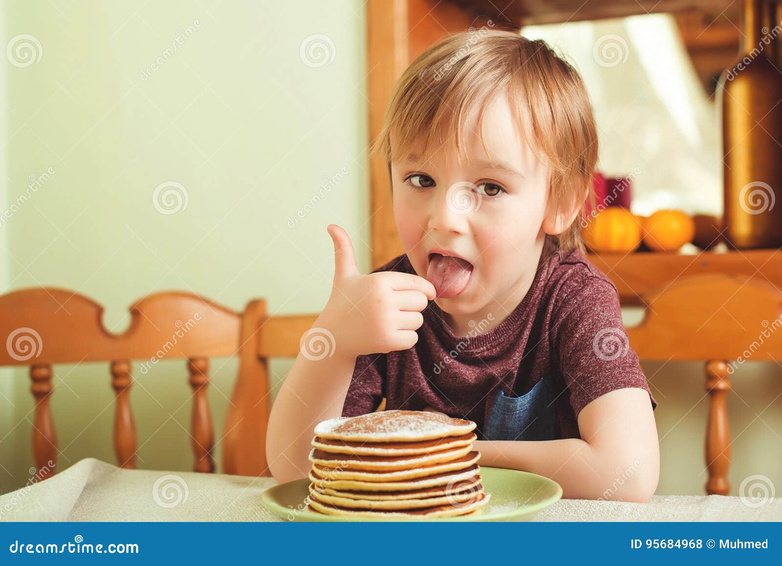 Cute Little Boy Eating A Stack Of Pancakes In The Kitchen Stock Photo