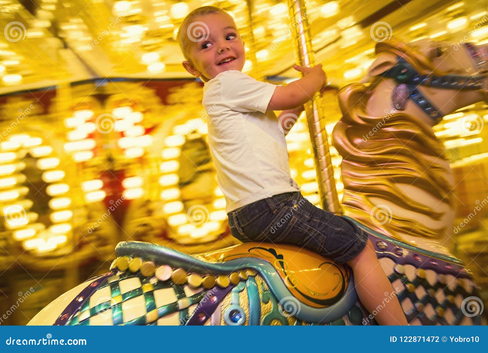 Happy Little Boy Riding A Merry Go Round Carousel With Bright Lights