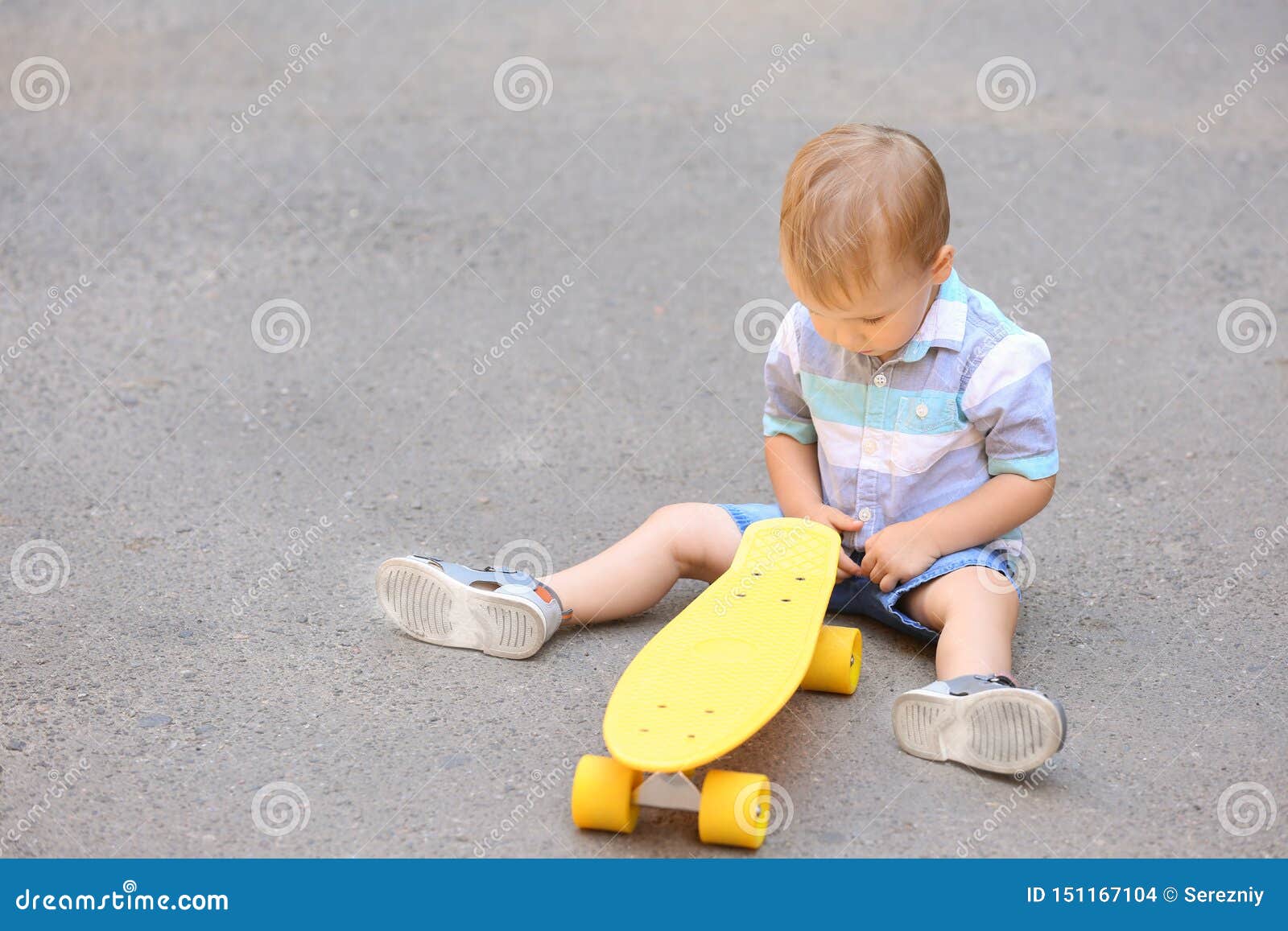 Cute Little Boy with Skateboard Sitting on Ground Outdoors Stock Photo