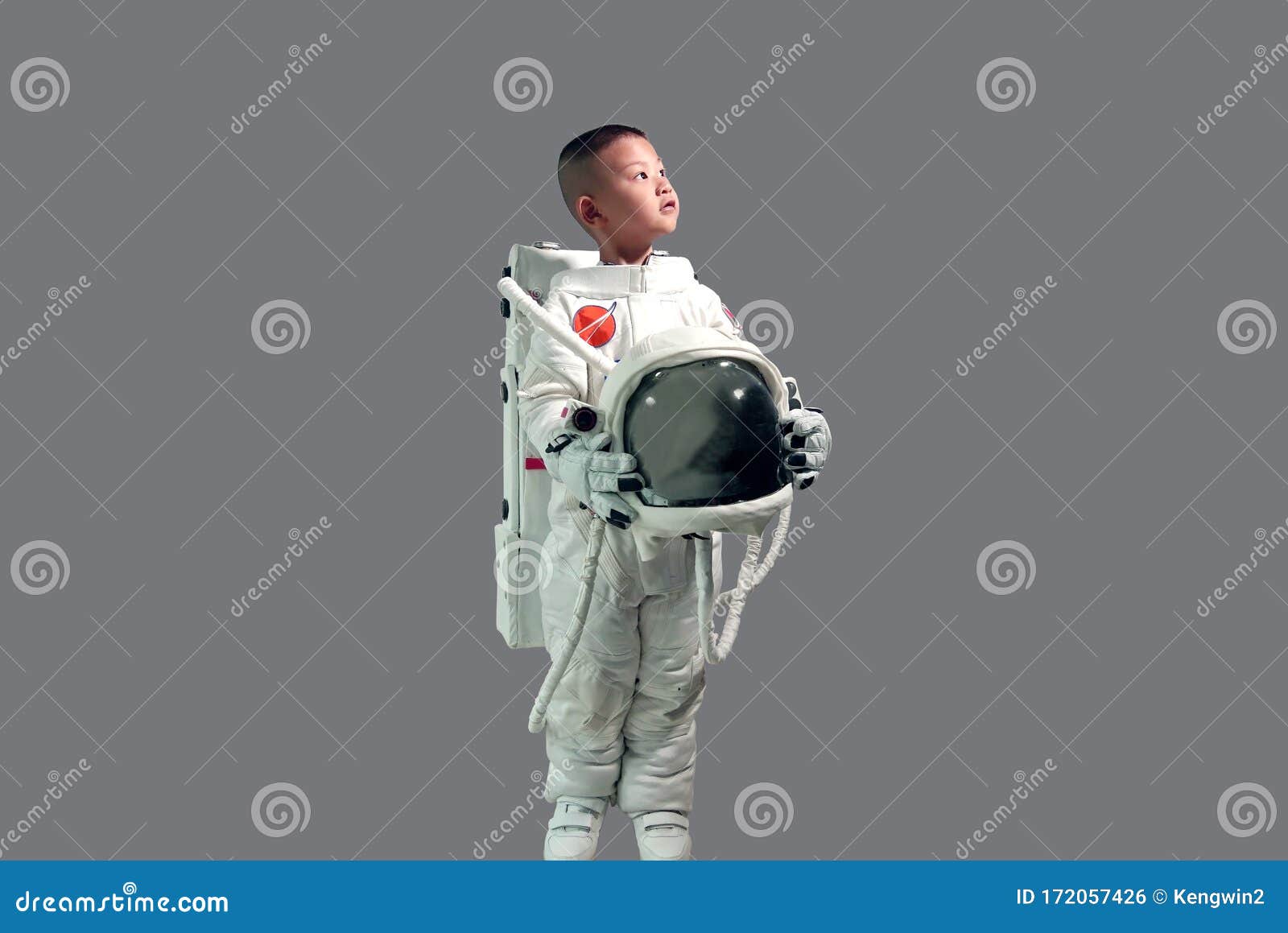 cute little boy in space suit holding helmet and standing looking up at the sky.