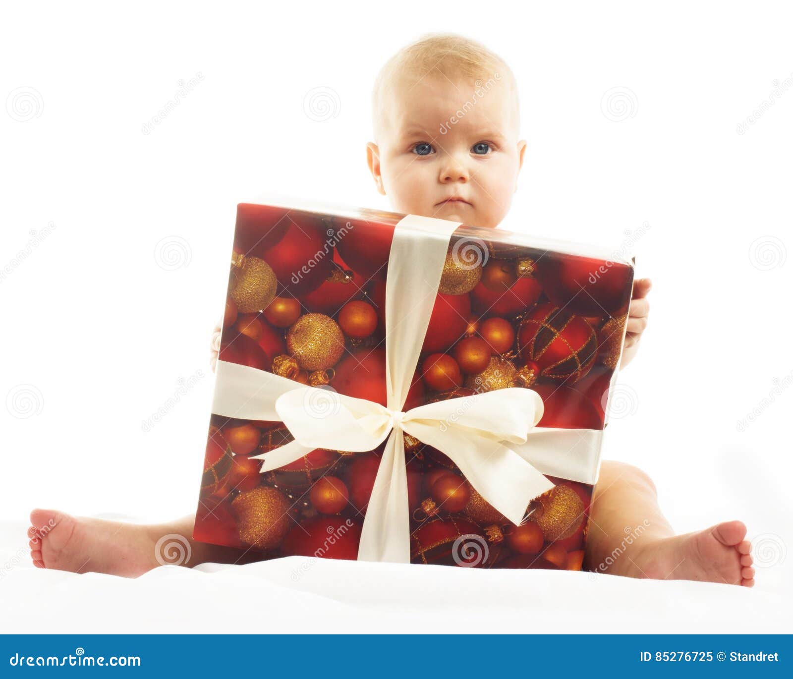 Cute baby who is trying to open a small Christmas present isolated on white background