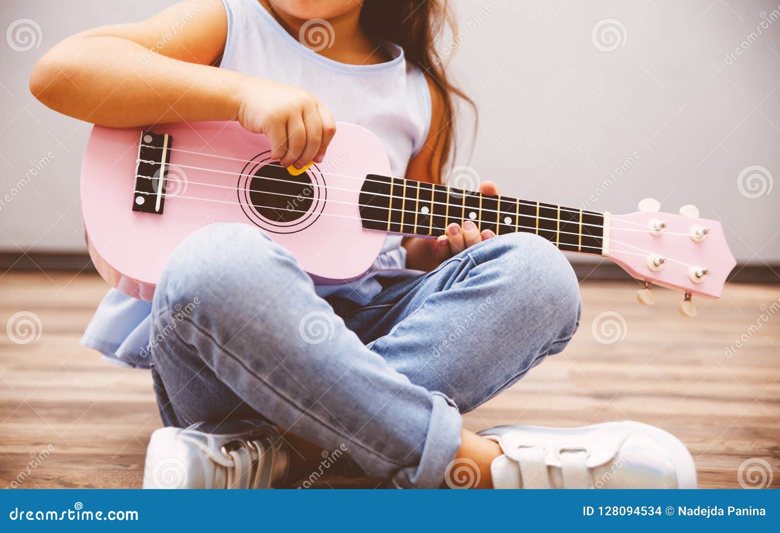 cute little girl playing pink ukulele sitting on floor