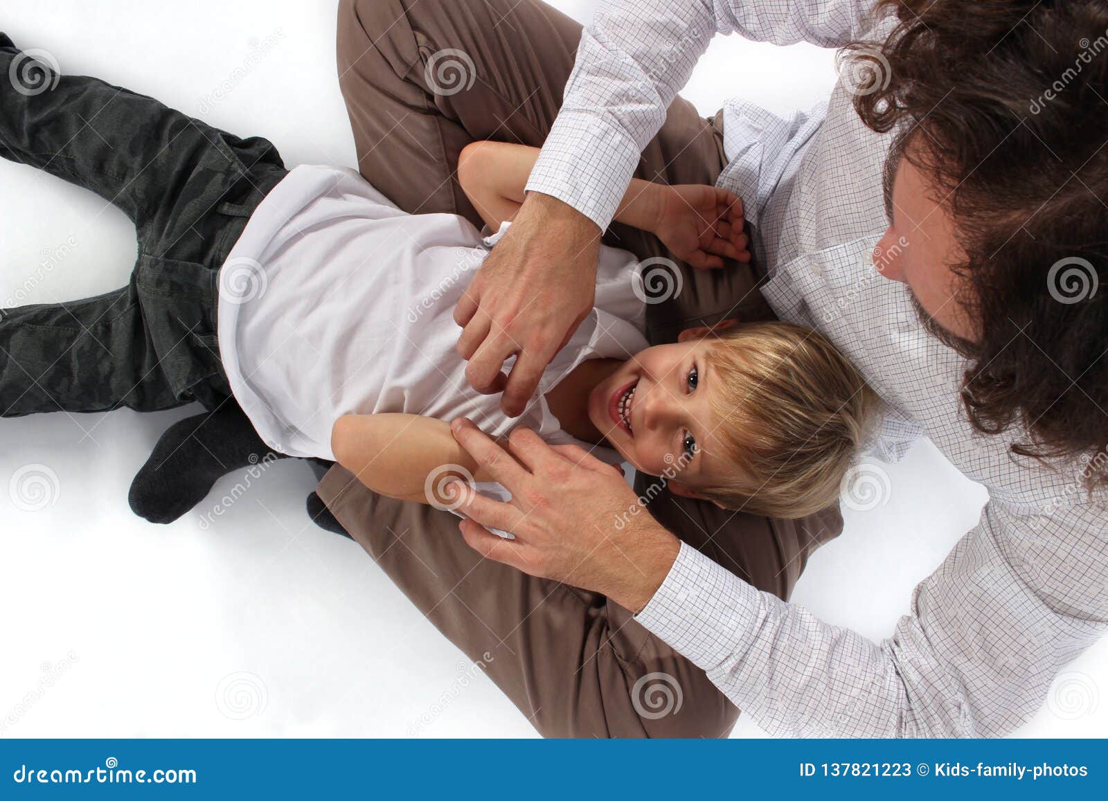 cute lovely little boy getting tickled by his daddy in his lap and smiling