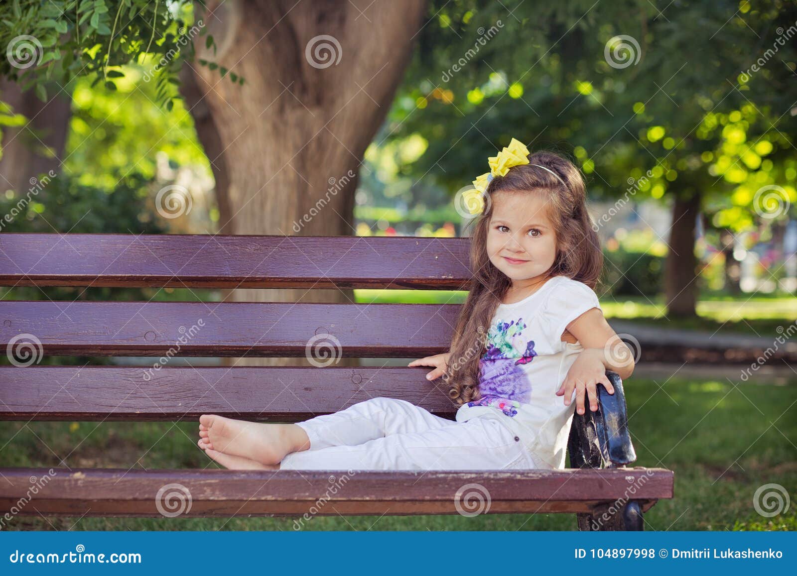 cute musical baby child girl with brunette hairs and stylish wear enjoying life sitting on wooden chair bench in summer awesome pa