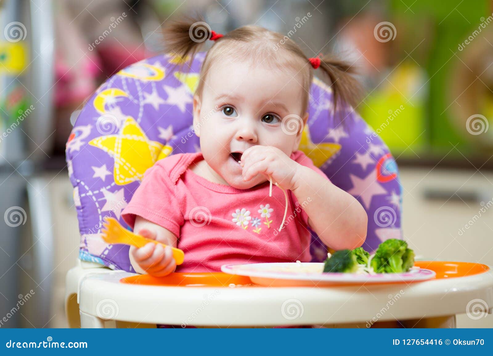 Cute One Year Old Baby Girl In Highchair With Pasta In Kitchen At