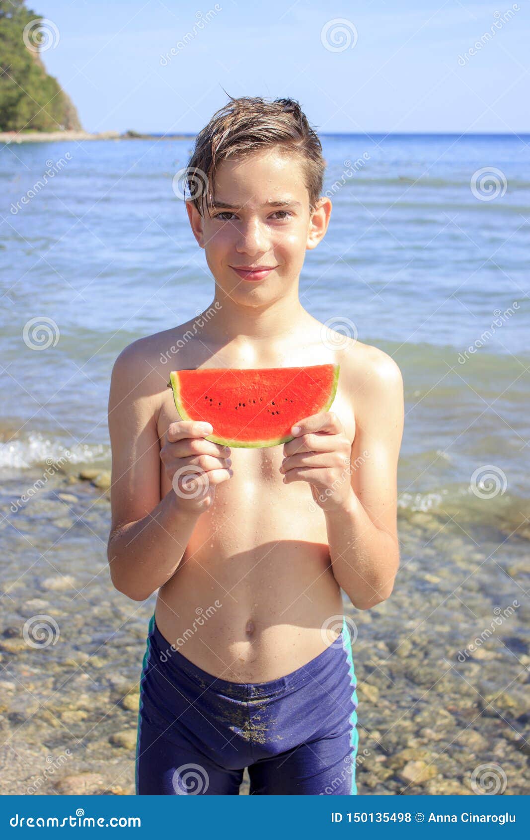 cute teenager boy holds a slice of watermelon on the beach by the sea
