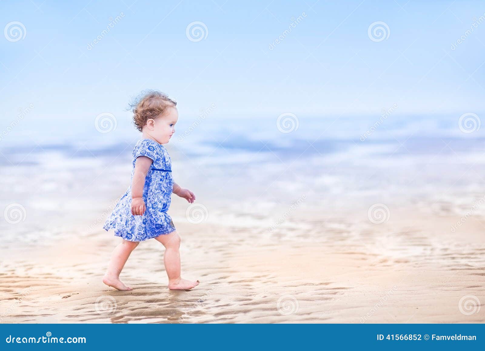 cute toddler girl in blue dress walking on beach