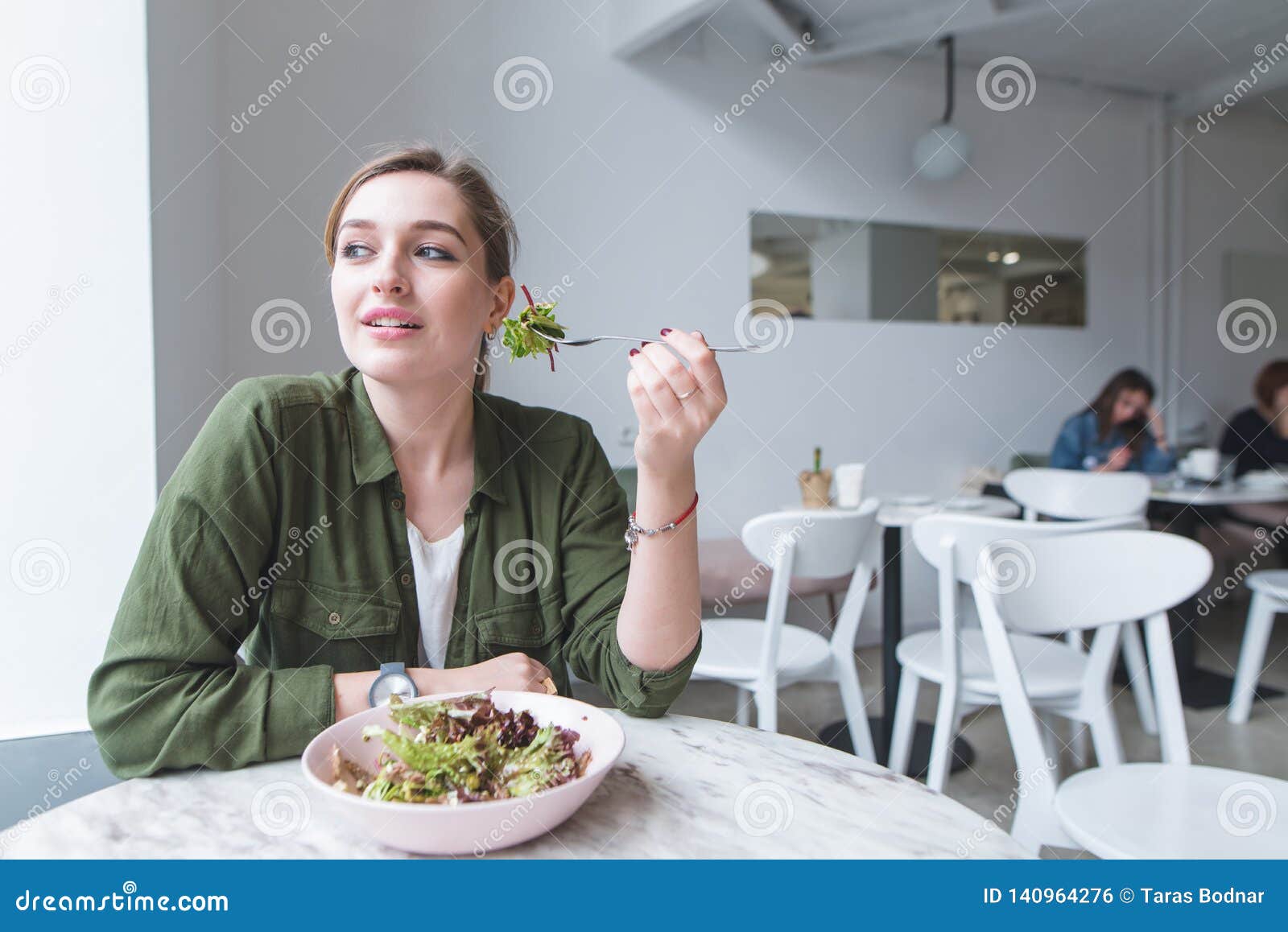 Cute Young Girl Sits in a Cozy Light Restaurant, Eating Salad and