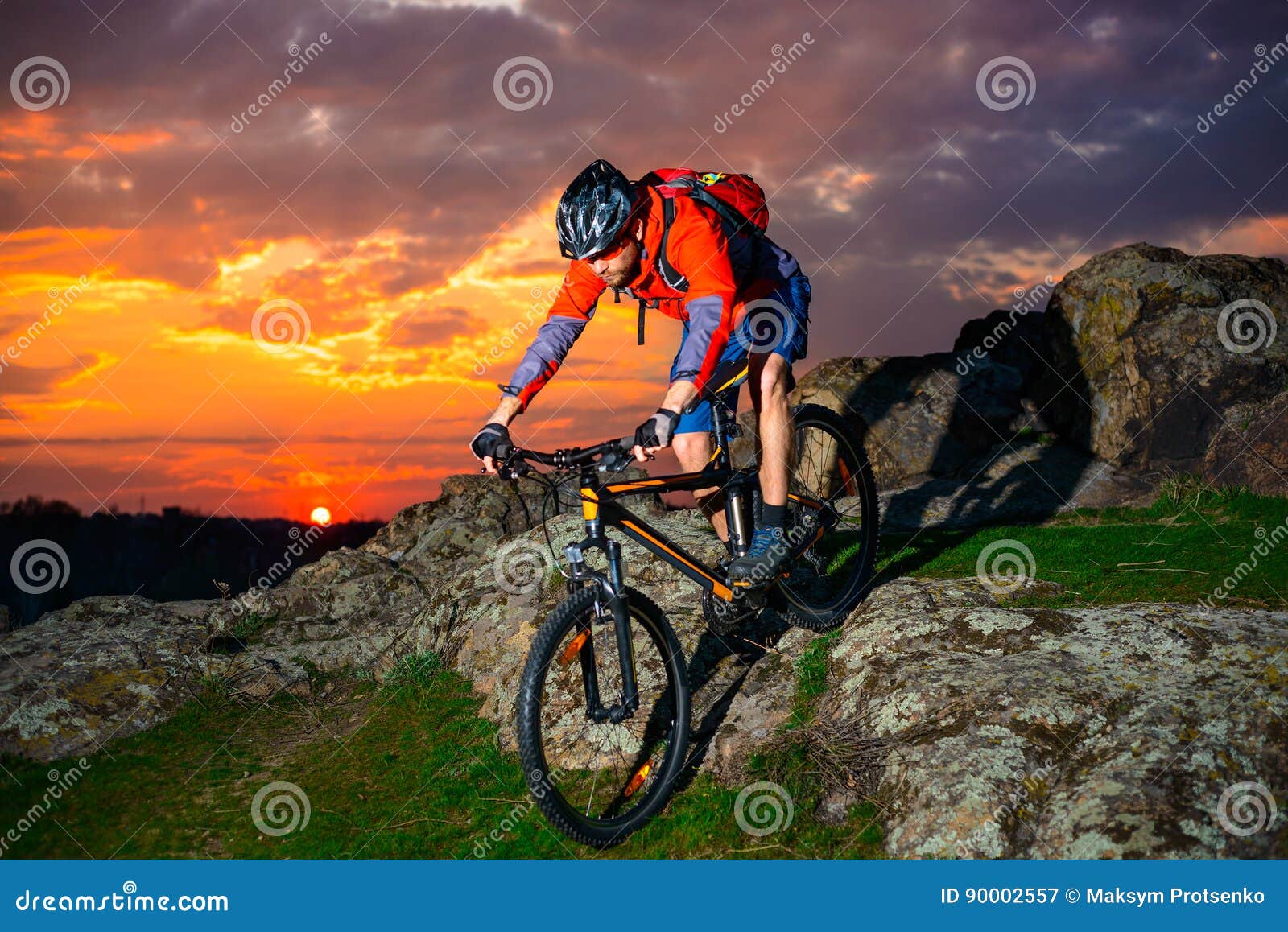 cyclist riding mountain bike down spring rocky hill at beautiful sunset. extreme sports and adventure concept.