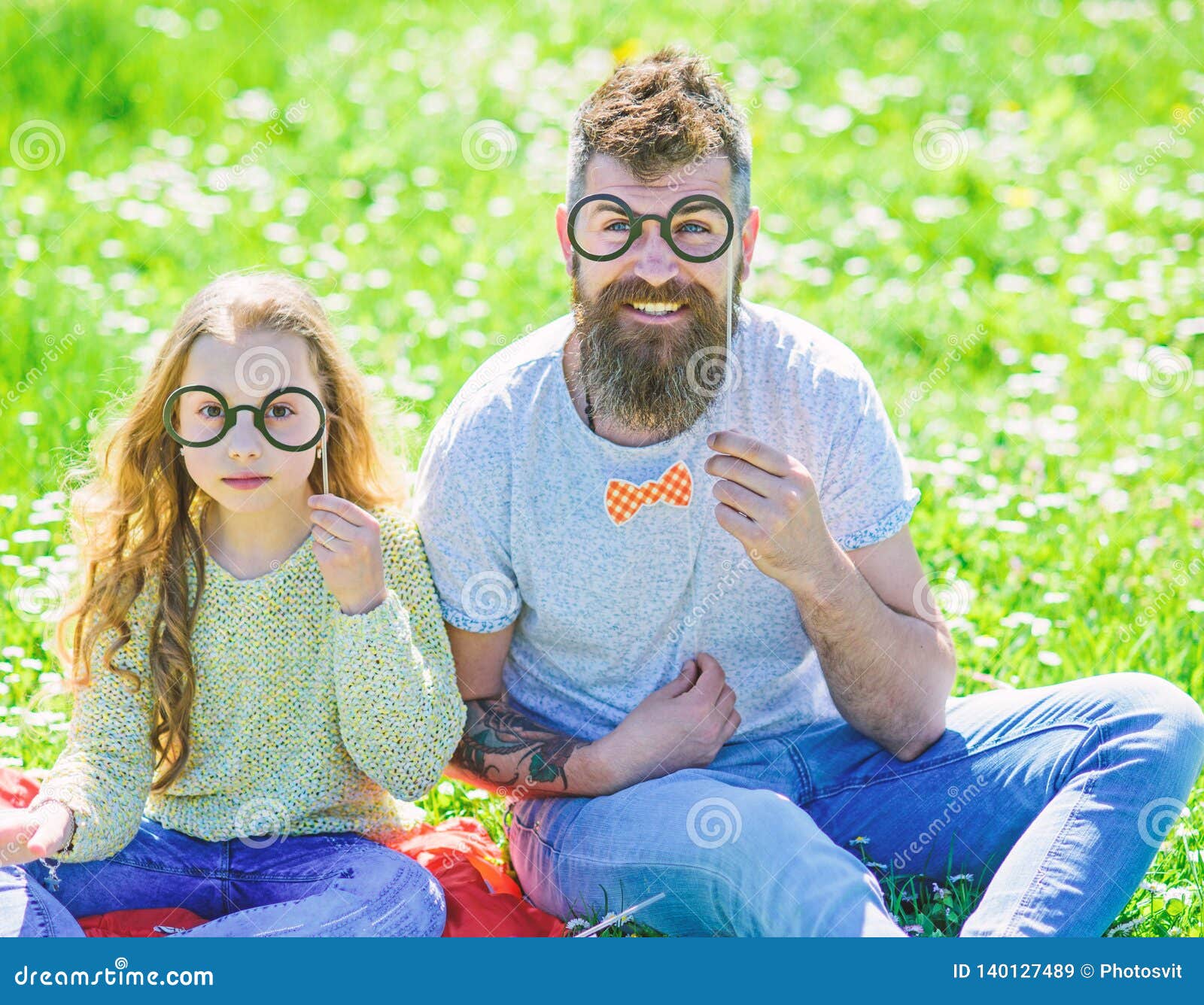 dad and daughter sits on grass at grassplot, green background. child and father posing with eyeglases photo booth