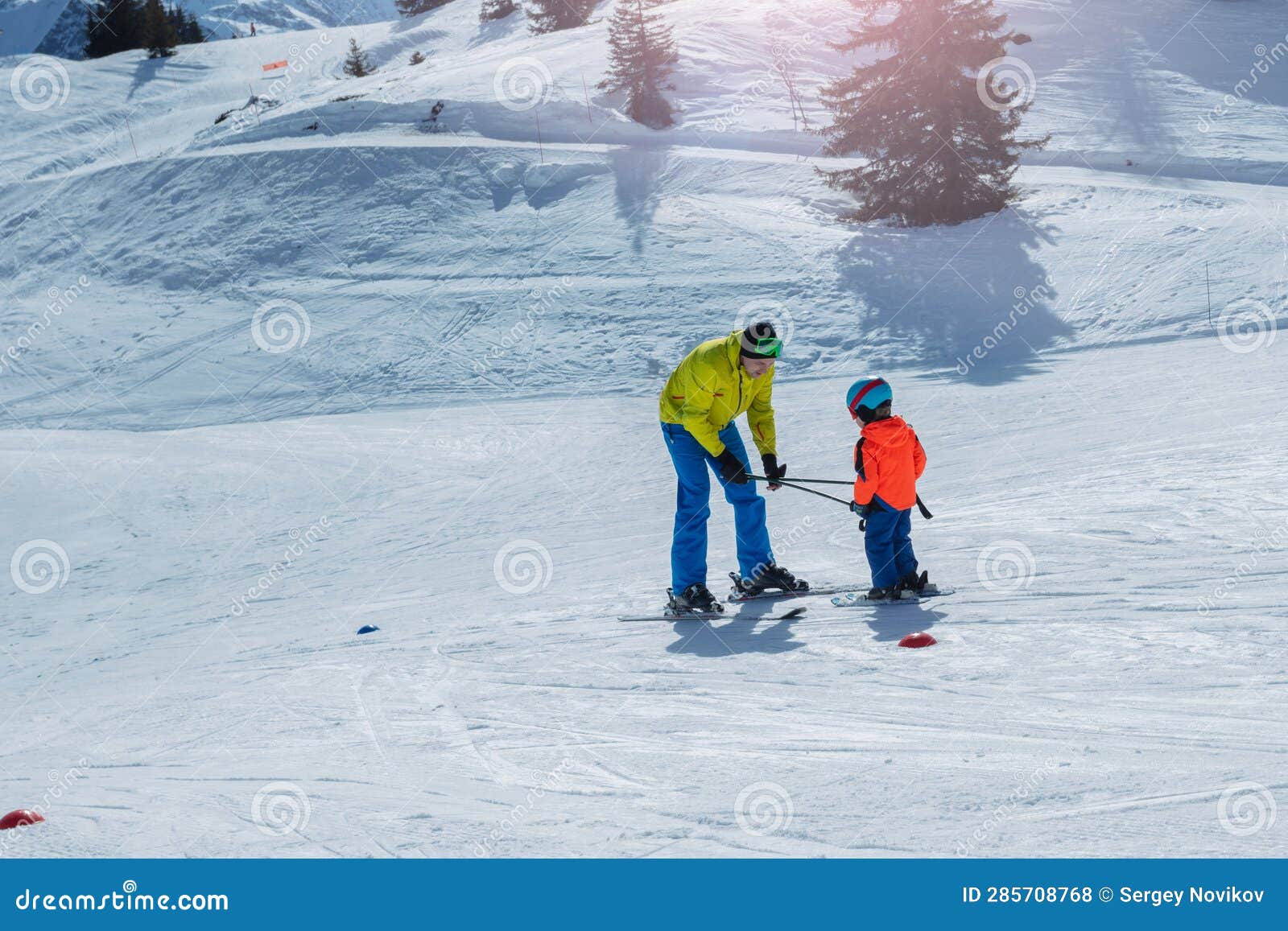 dad glide backwards teaching little child to ski using poles