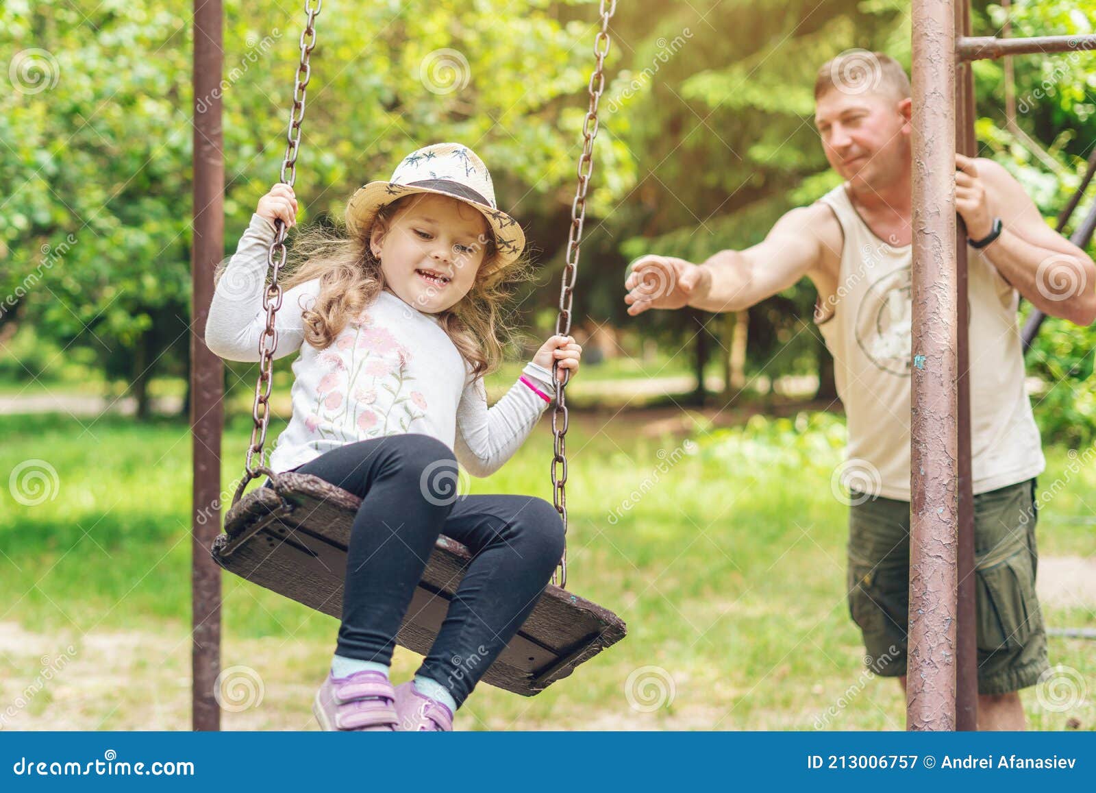 Dad Swings His Little Happy Daughter on a Swing on a Warm Sunny Day