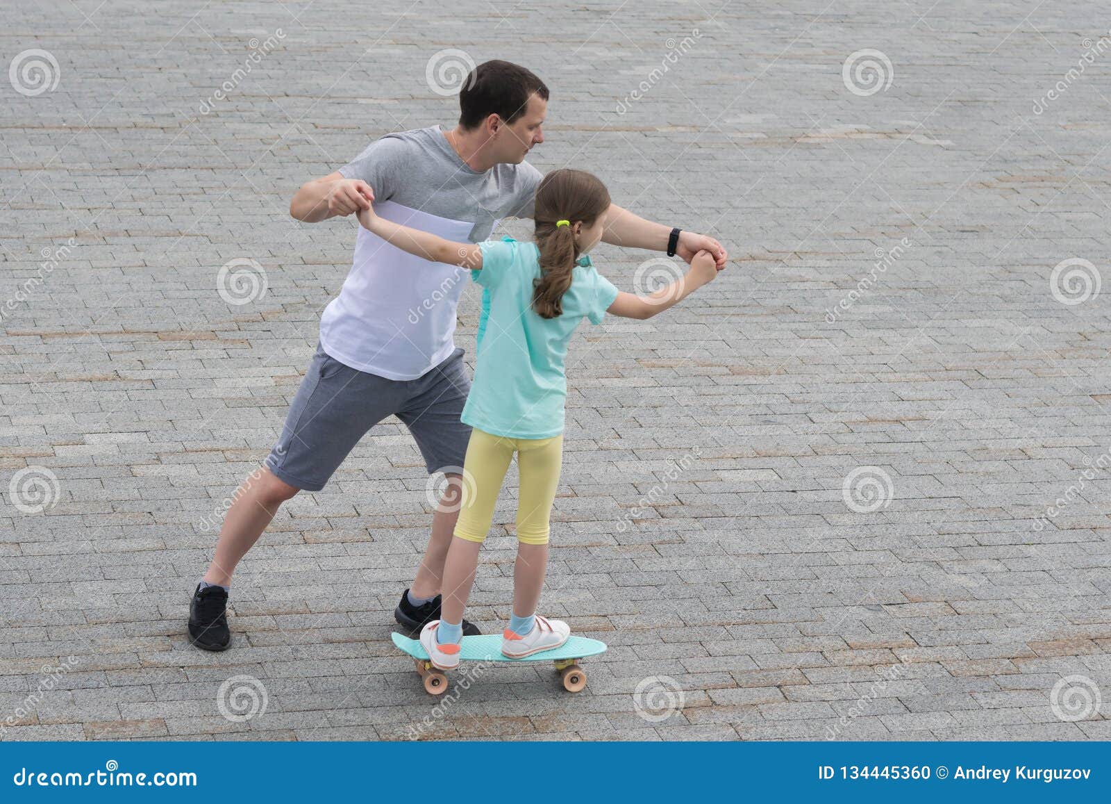 dad teaches daughter to skateboard in a city park