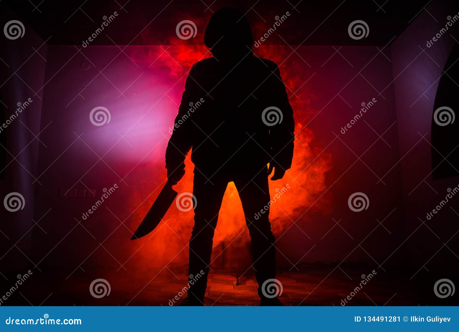 a dangerous hooded man standing in the dark and holding a knife. face can not be seen. committing a crime concept. selective focus