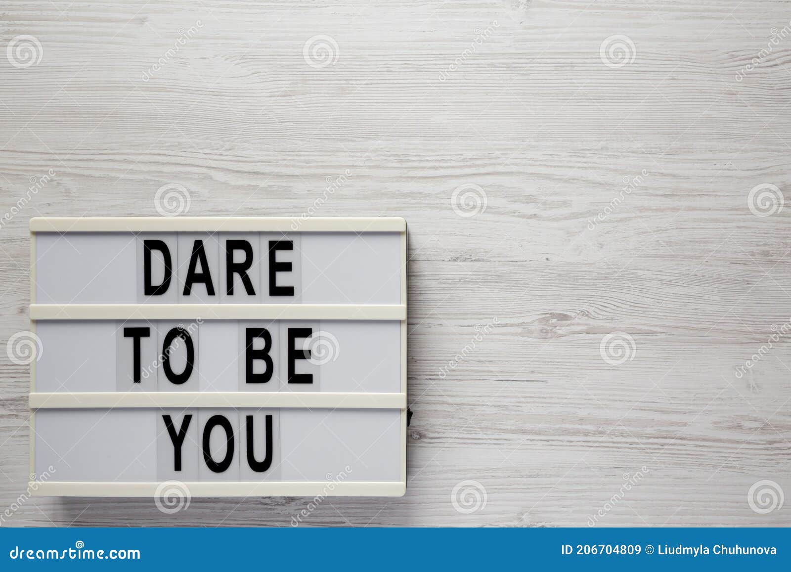 `dare to be you` on a lightbox, cliboard with blank sheet of paper on a white wooden surface, top view. flat lay, overhead, from