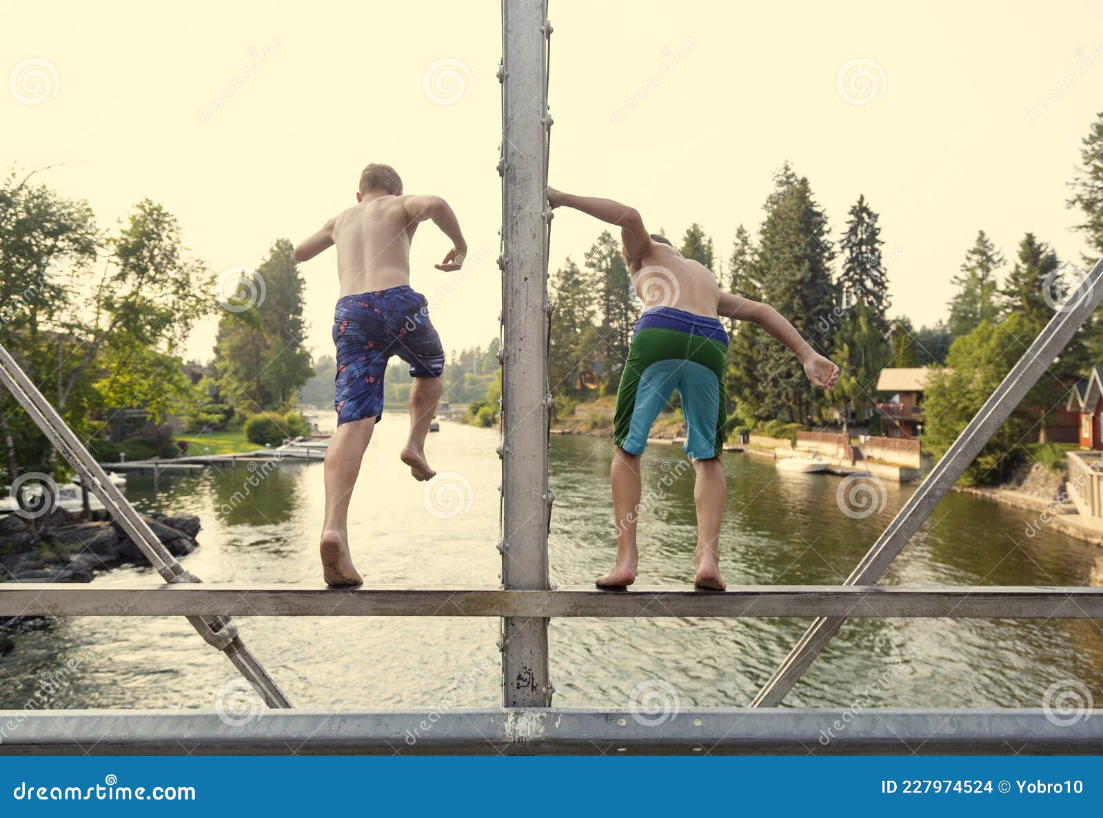 daring young boys jumping off a bridge into the river. view from behind.
