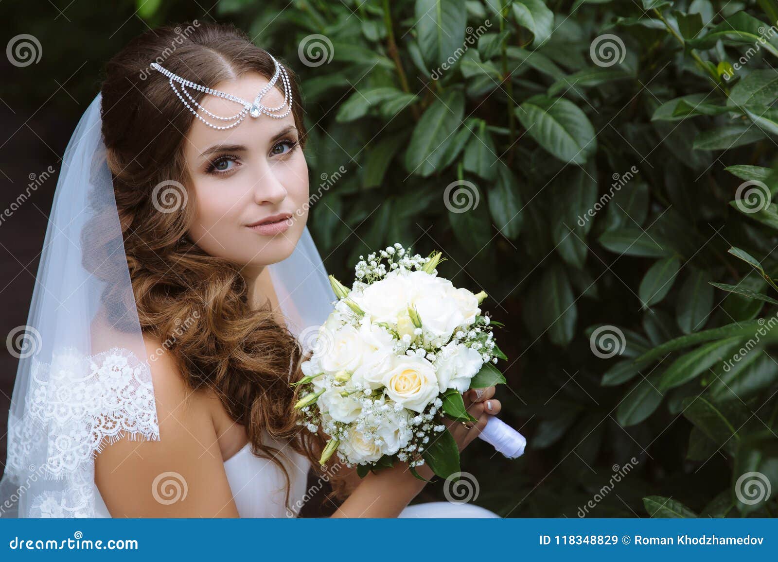 A Dark-haired Bride with Curly Hair Poses Against a Green Background in ...