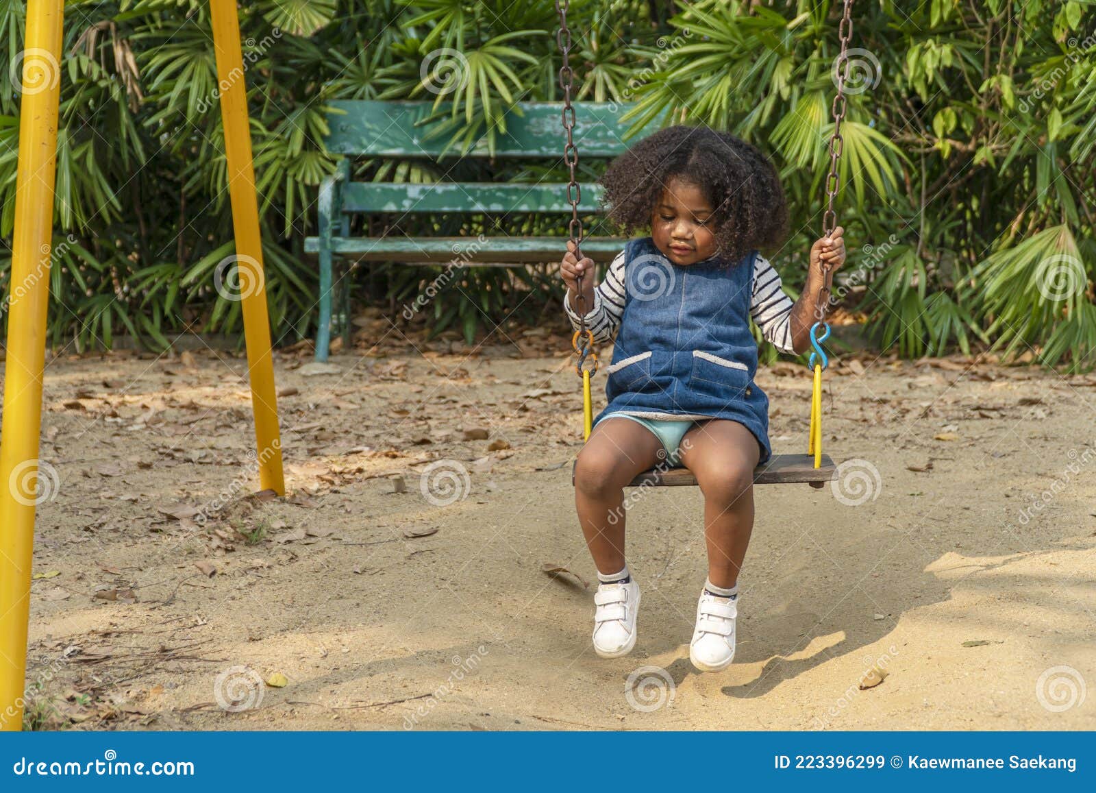 dark skinned toddler daughter mixed-race playing swing in playground while looking something at pubic park