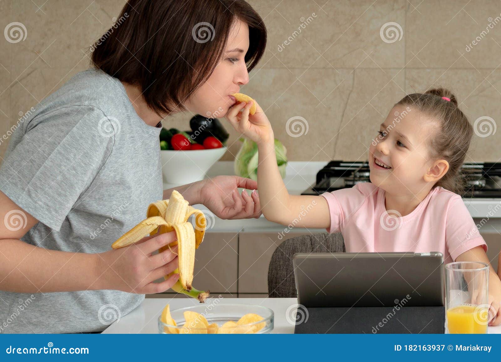 Daughter Feeding Mother with Potato Chips in Kitchen Stock Image
