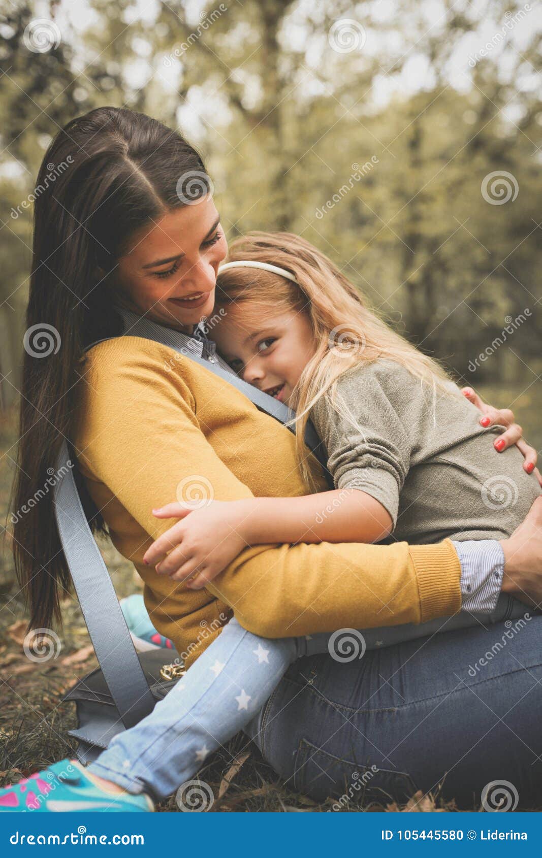 daughter sitting in mothers lap at city park.