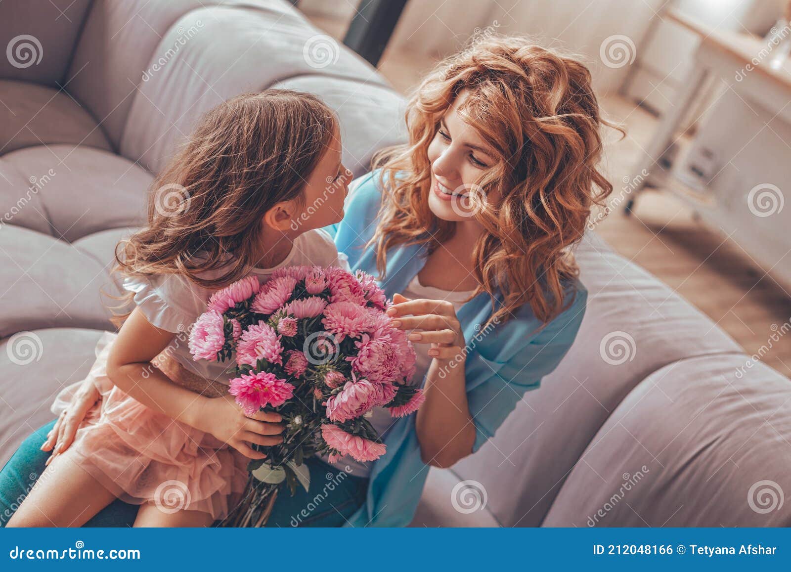 daughter sitting on mothers laps with bouquet of flowers on the sofa and looking at each other