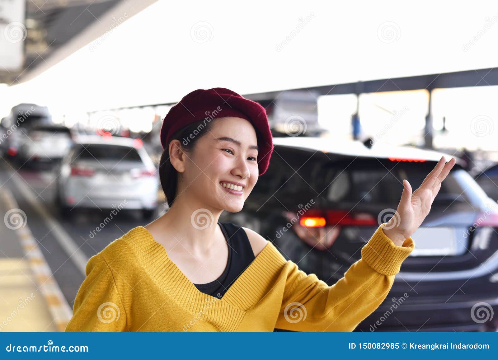 De Aziatische vrouw roept de dienst van de taxiauto bij de luchthaven, Vrolijk meisje die en haar hand, Hello-gebaar glimlachen golven