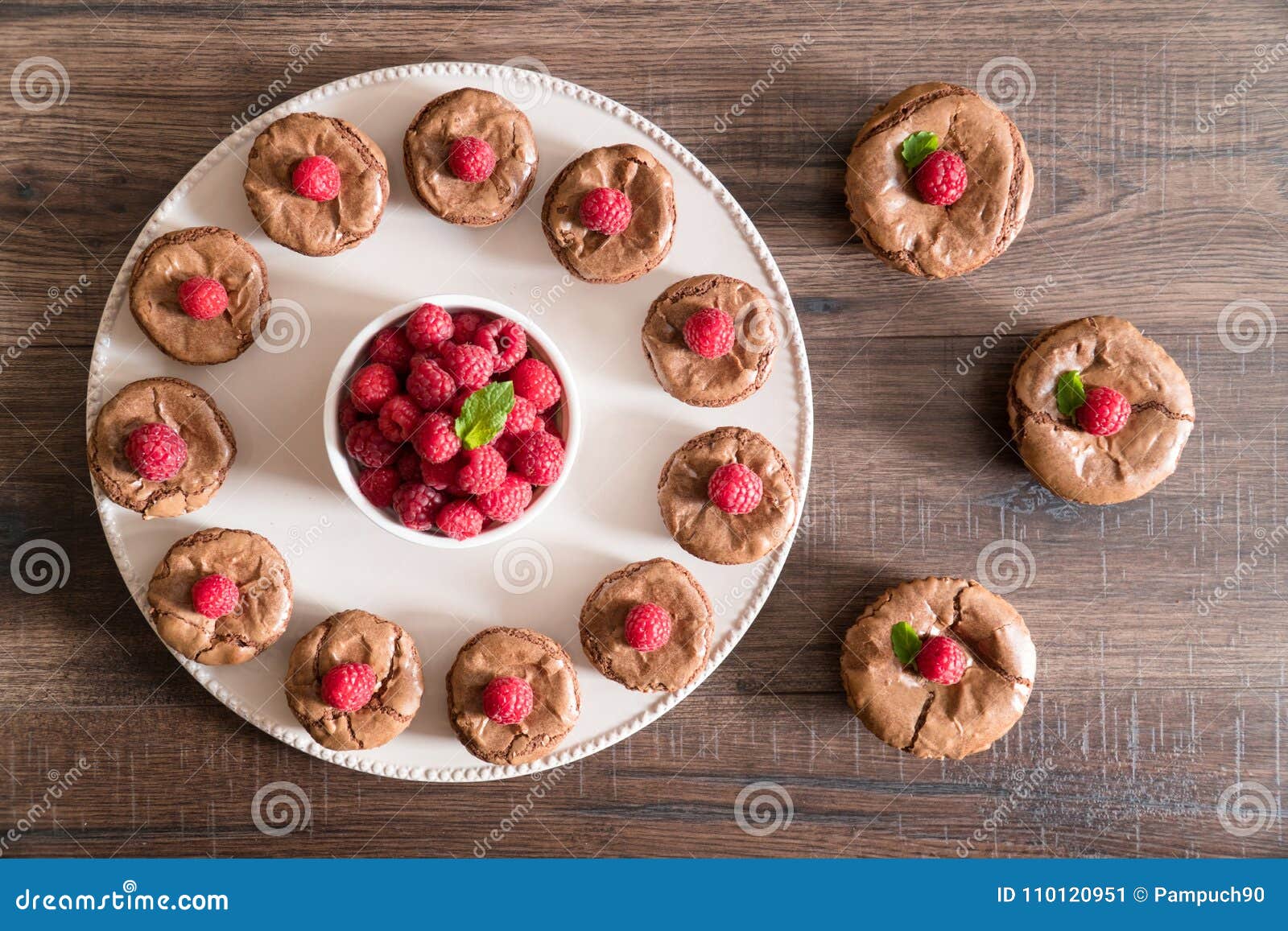 De cakes van de chocoladelava met verse frambozen en munt. De heerlijke cakes van de chocoladelava met verse die frambozen en munt, in een cirkel op de porcelan plaat op de houten lijst met witte kom van frambozen in het midden worden geschikt