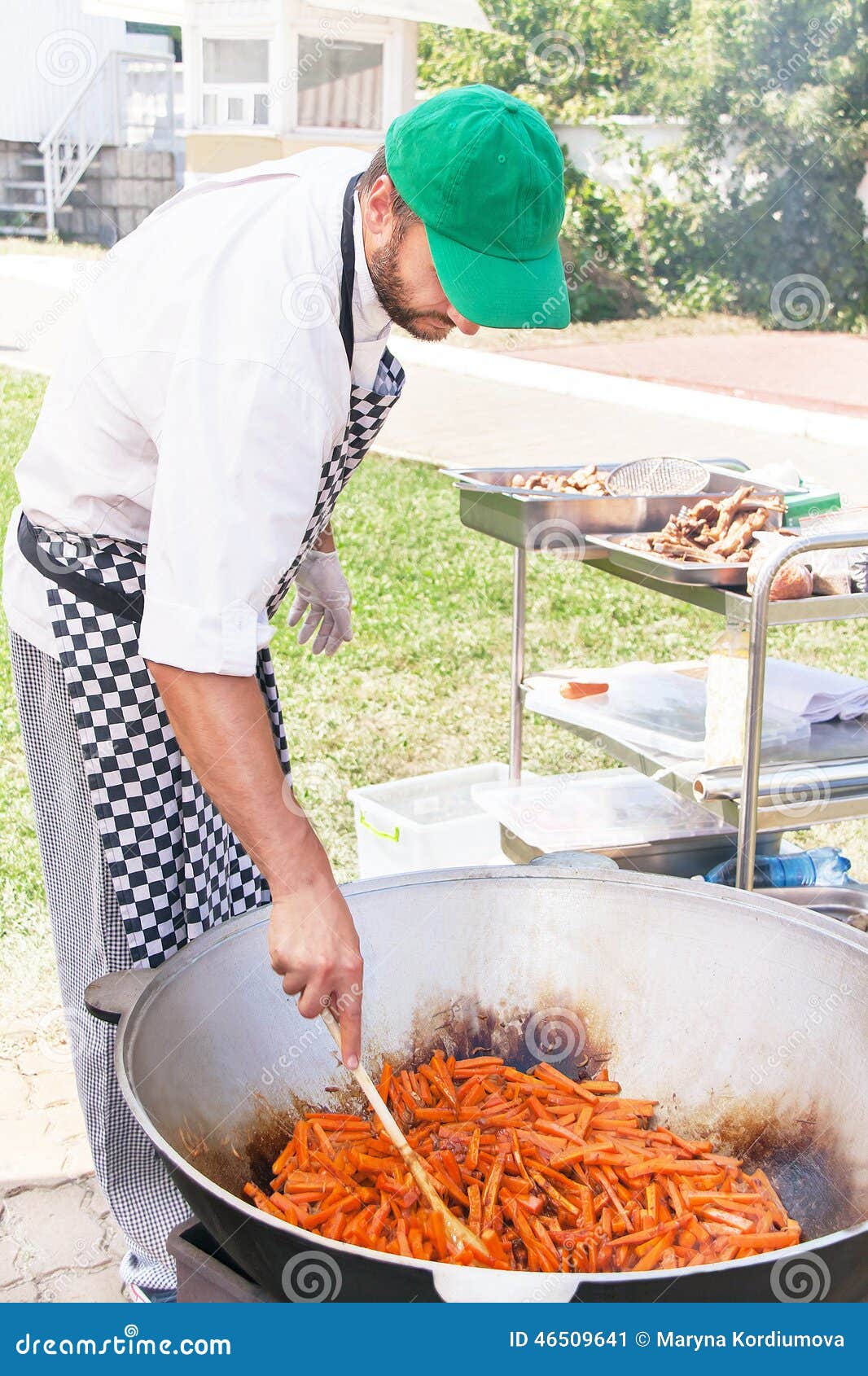 De chef-kok kookt heerlijke groenten in de ketel op brand. Kyiv, de Oekraïne â€ „3 Augustus, 2014 De chef-kok kookt in openlucht heerlijke groenten in de ketel op brand bij een gebeurtenis Kaukasisch mannetje die voedsel voor gezonde etende mensen in de de zomer zonnige dag maken