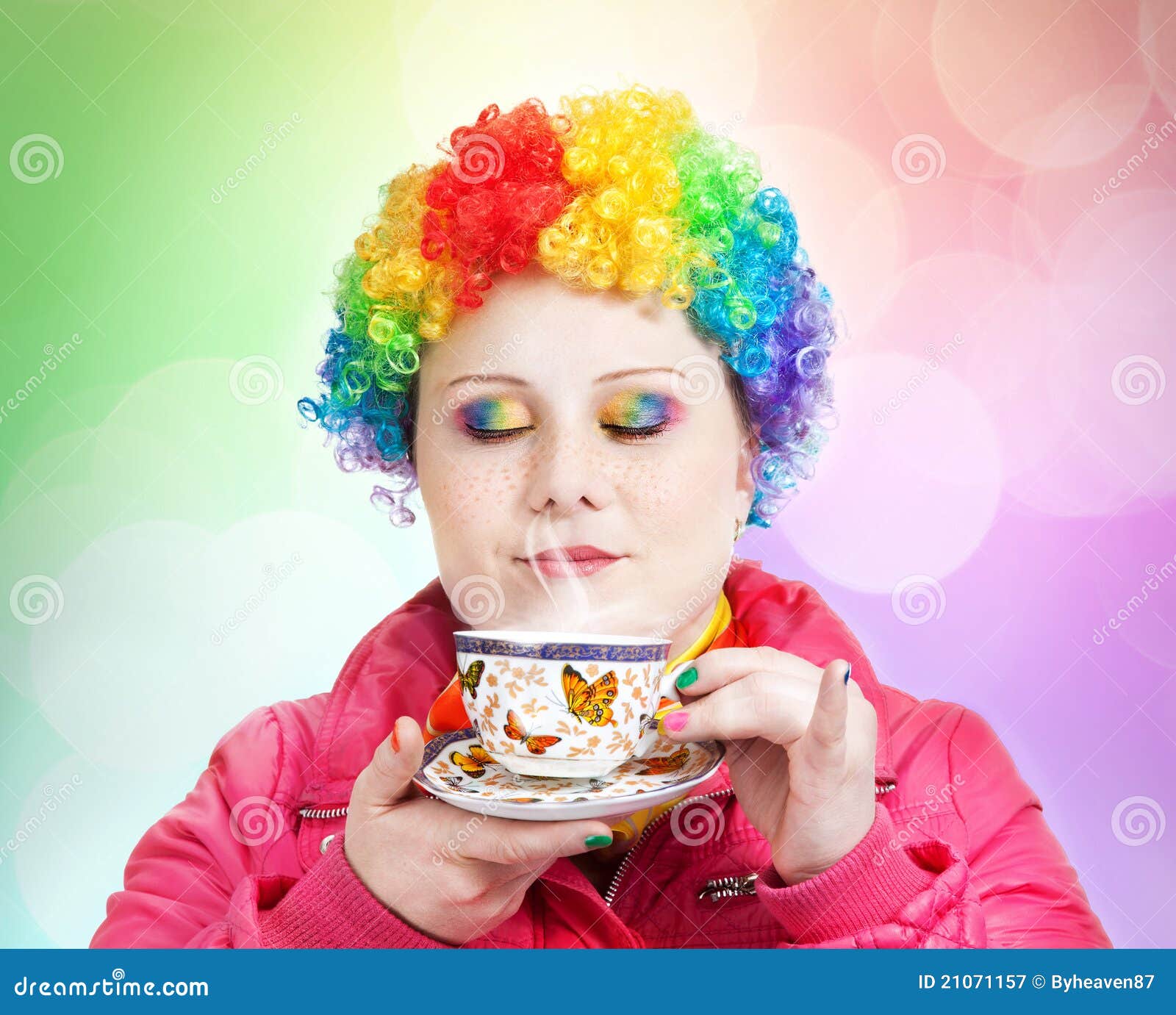 De Clown van de regenboog met kop thee. De clown in regenboogpruik en de creatieve regenboog maken holding kop thee en ademhaling in de stoom bij multicolored bokehachtergrond op