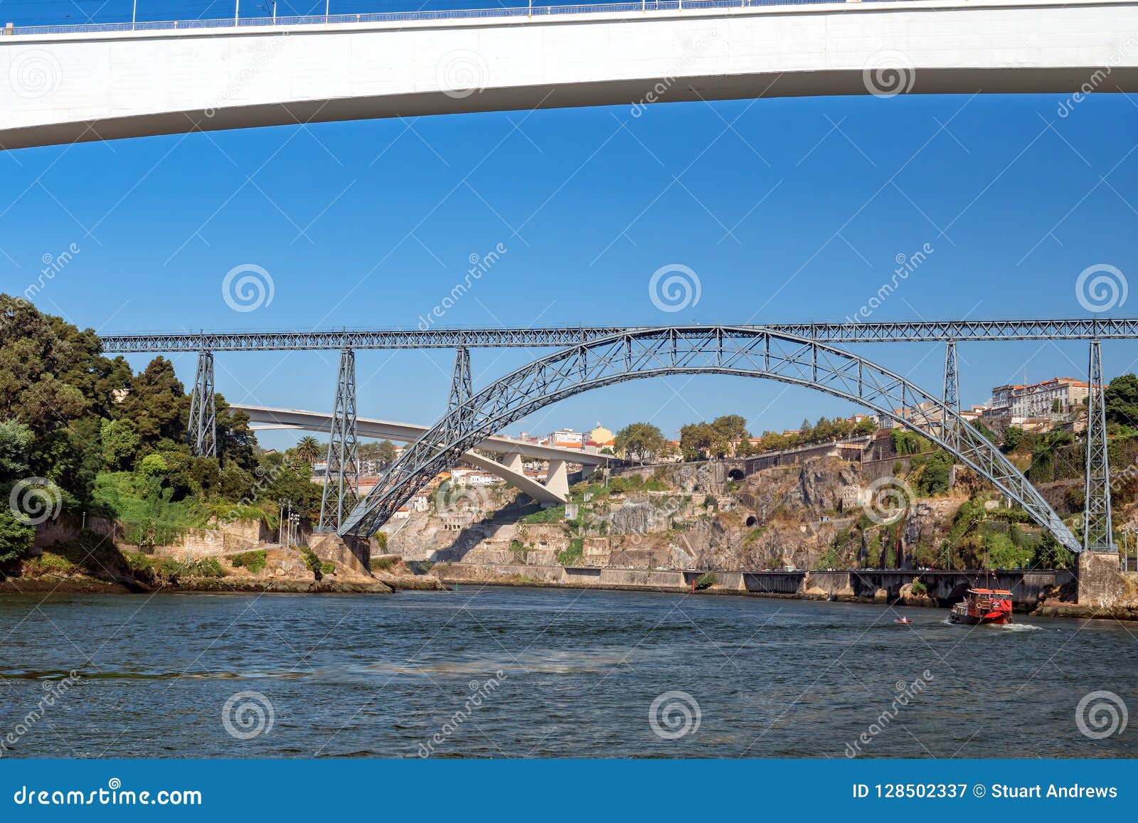 De Cruise van de zes Bruggenrivier, Porto, Portugal. Een mening van een bootrubriek onderaan rivier naar Porto en Gaia tijdens een Zes Bruggencruise op de Rivier Douro De boot gaat onder de St John ` s Brug over, naderen Ponte DE Sao Joao en de cruiseboot vooraan de staalstructuur Maria Pia Bridge, Ponte DE D Maria Pia, wat door Gustave Eiffel werd ontworpen Ponte-Infante D Henrique Bridge, Ponte-Infante D Henriqueis is de concrete brug in de afstand