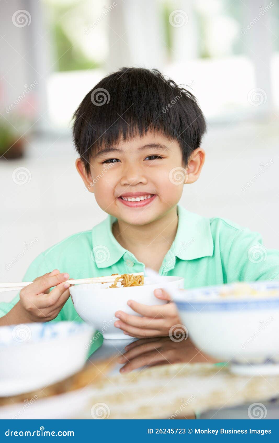 De jonge Chinese Zitting die van de Jongen thuis Maaltijd eet die bij Camera glimlacht