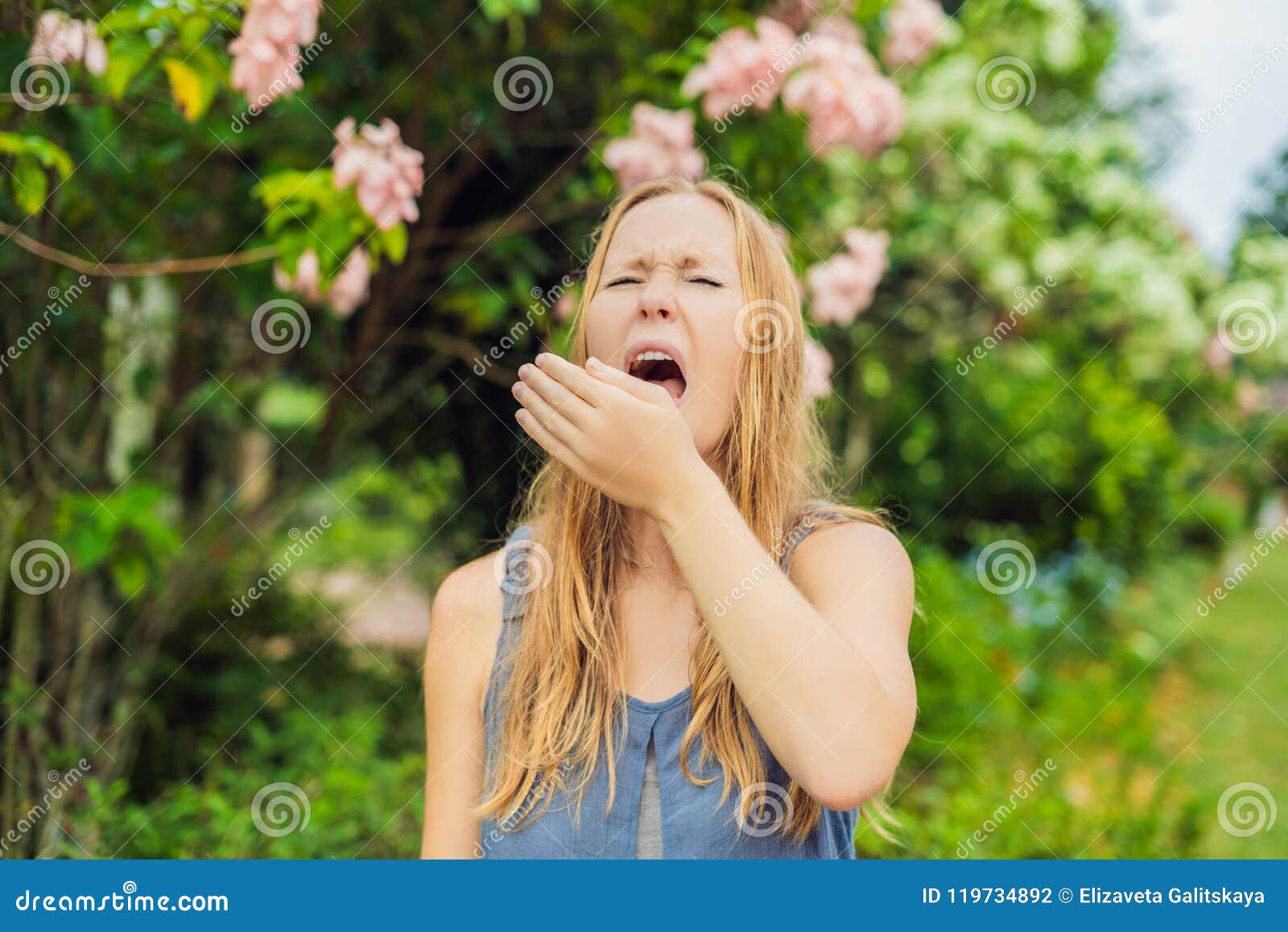 De jonge vrouw niest in het park tegen de achtergrond van een bloeiende boom Allergie voor stuifmeelconcept