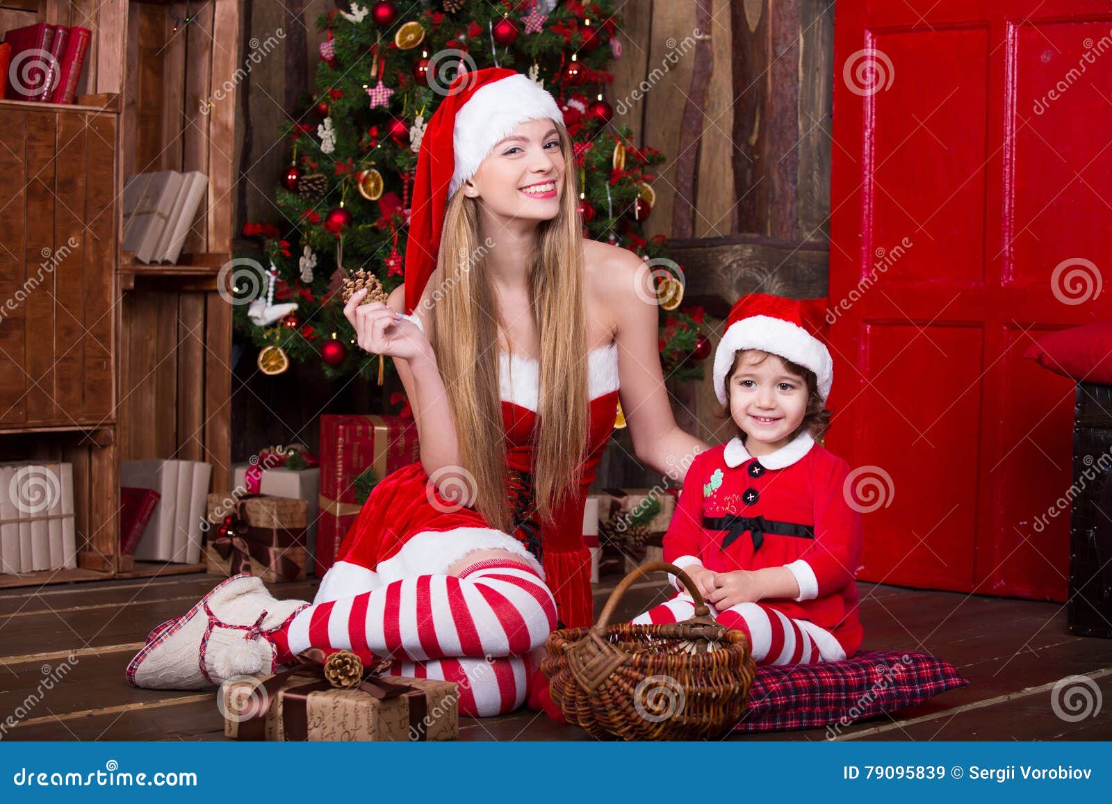 De Leuke Meisjes Die Zitten Met Stelt Dichtbij Kerstboom In Kerstmankostuums Voor Glimlachend