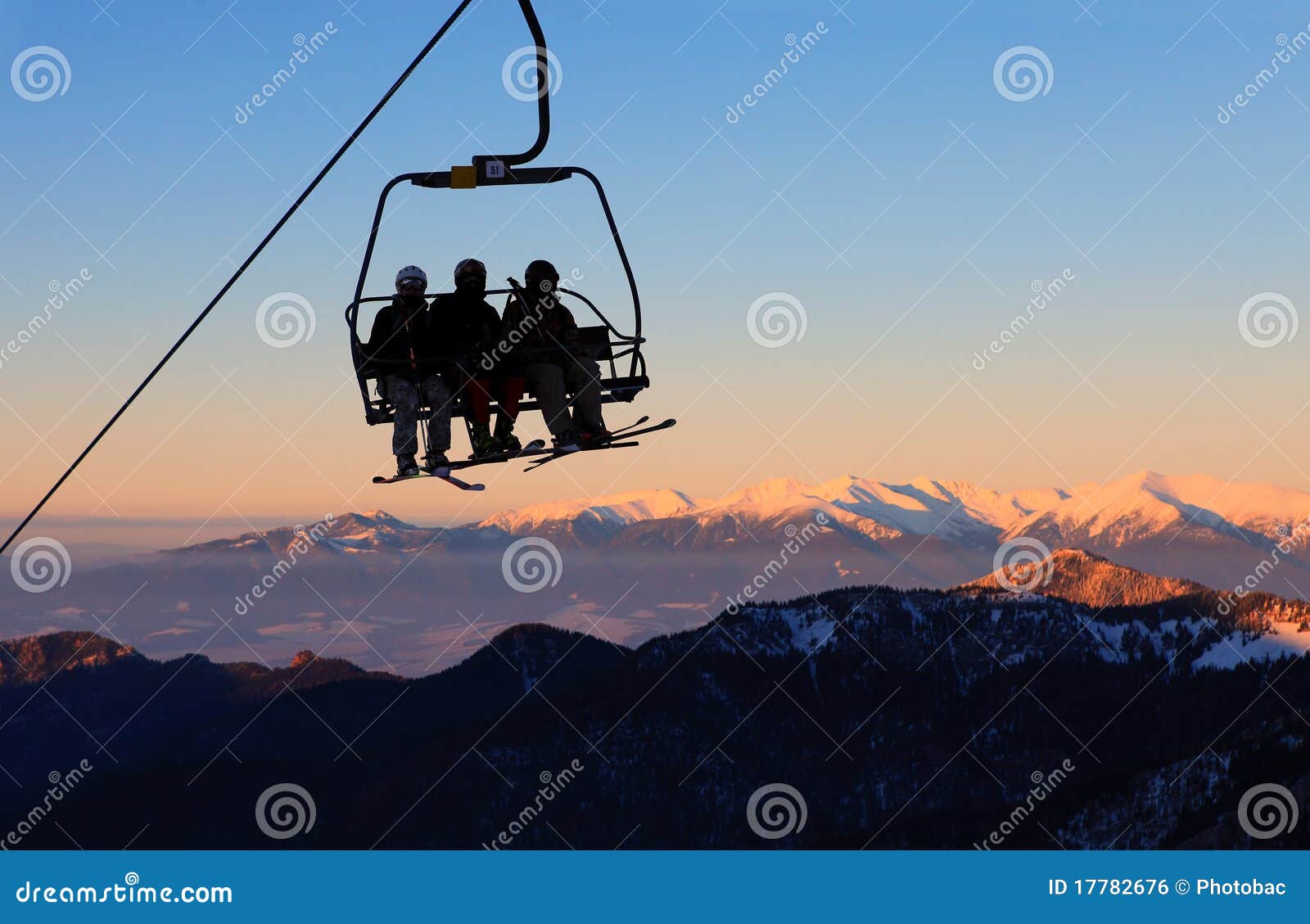 De skilift van de stoel met skiërs over blauwe hemel en bergen