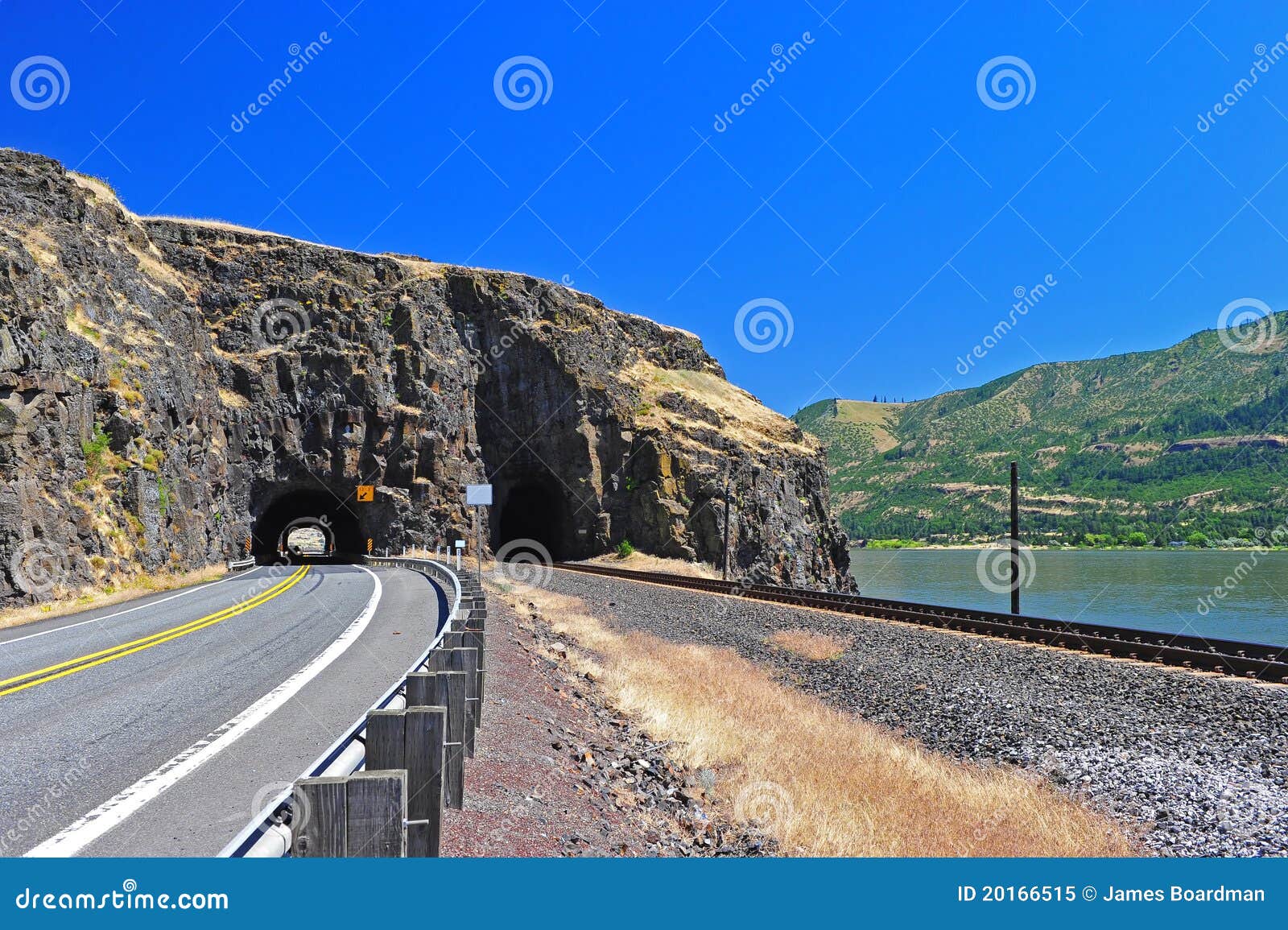 De sporen van de spoorweg en een weg komen uit een natuurlijke gezichts poorttunnel te voorschijn langs de Kloof van de Rivier van Colombia aan de de staatskant van Washington.