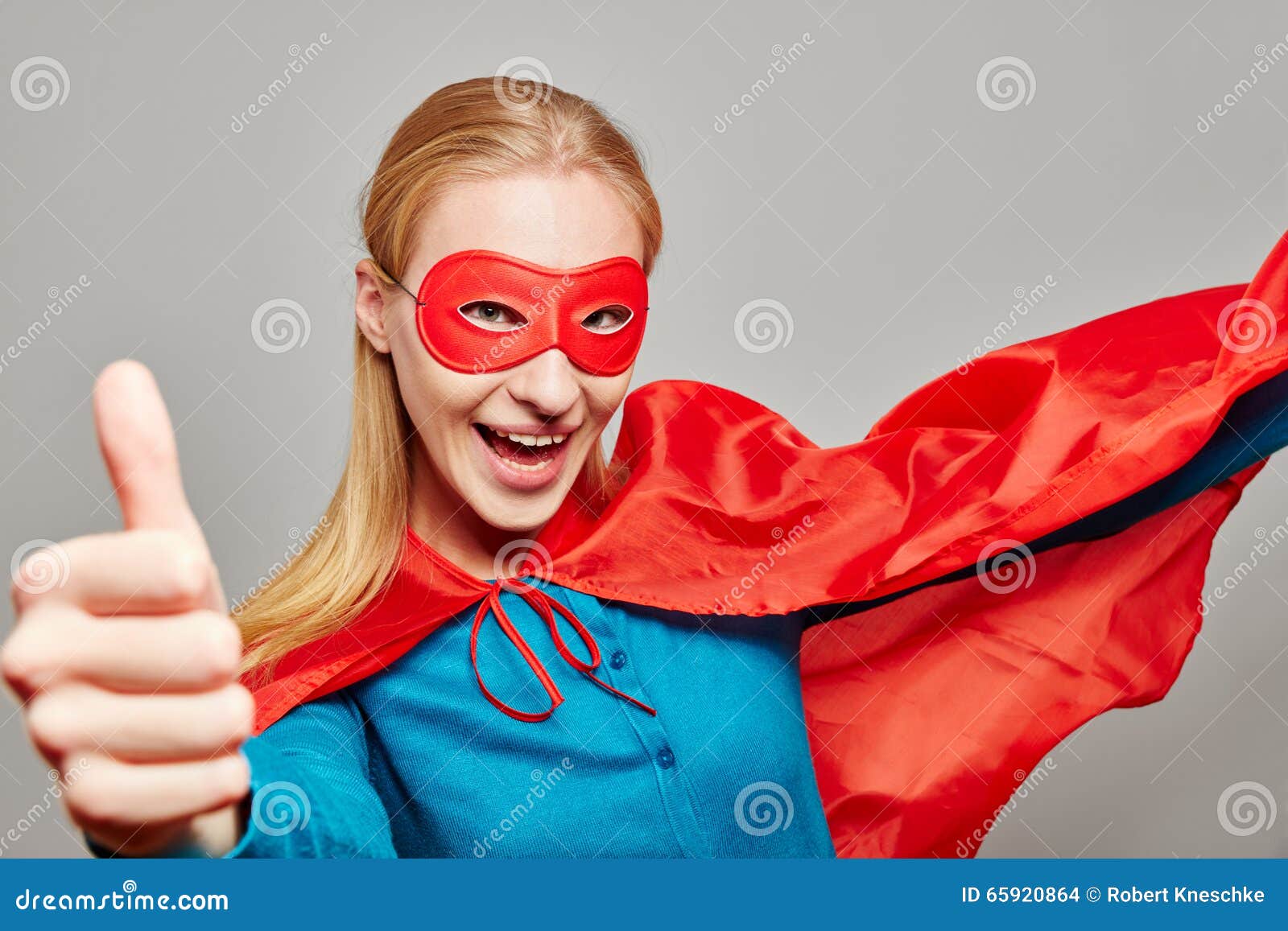 De vrouw kleedde zich als superhero met haar omhoog duim. De glimlachende vrouw kleedde zich omhoog als superhero tegenhoudend haar duim
