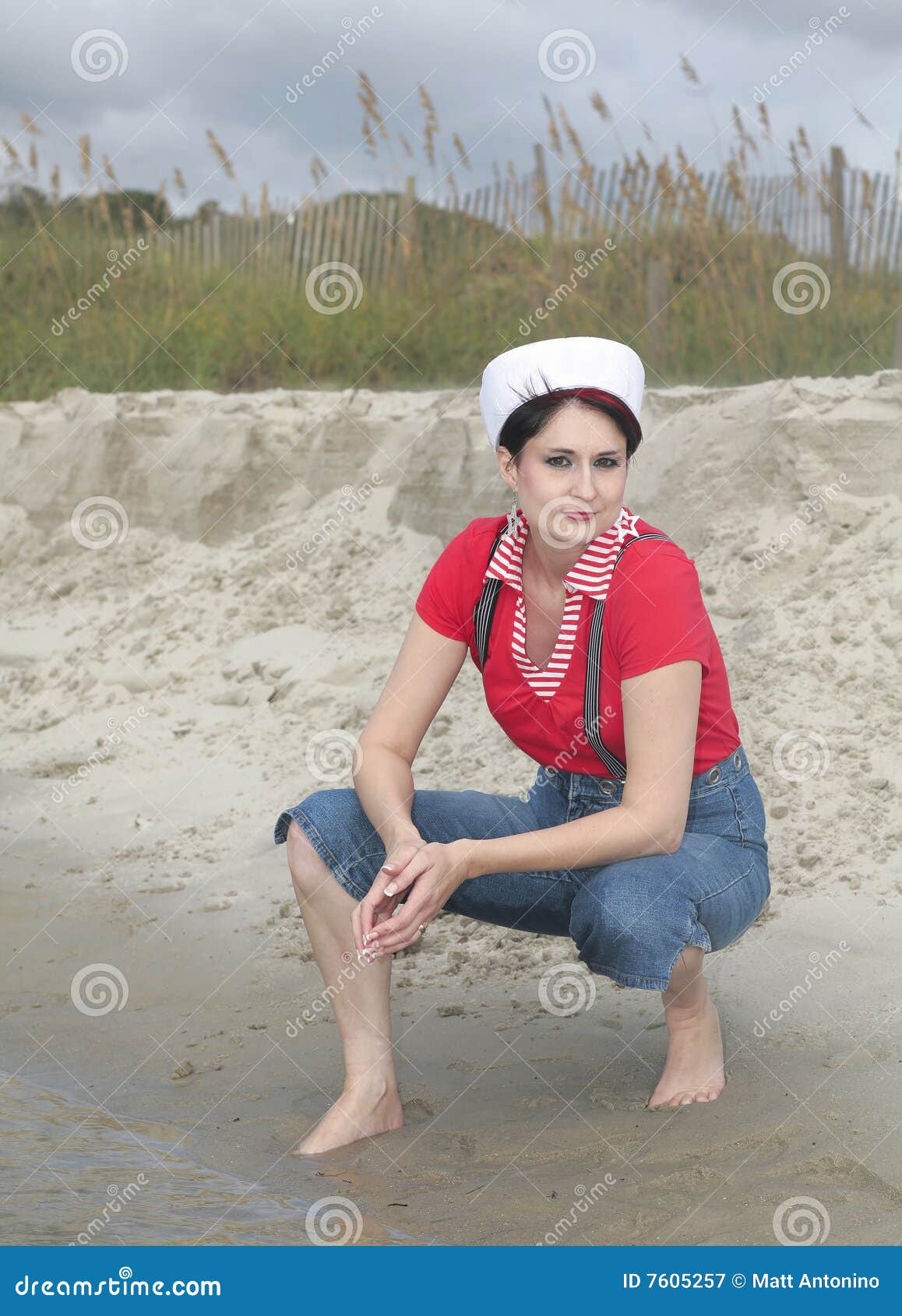De vrouw van de zeeman op het strand. Één mooie vrouw in het rode witte en blauwe zeevaartslijtage stellen op het strand dichtbij een duin