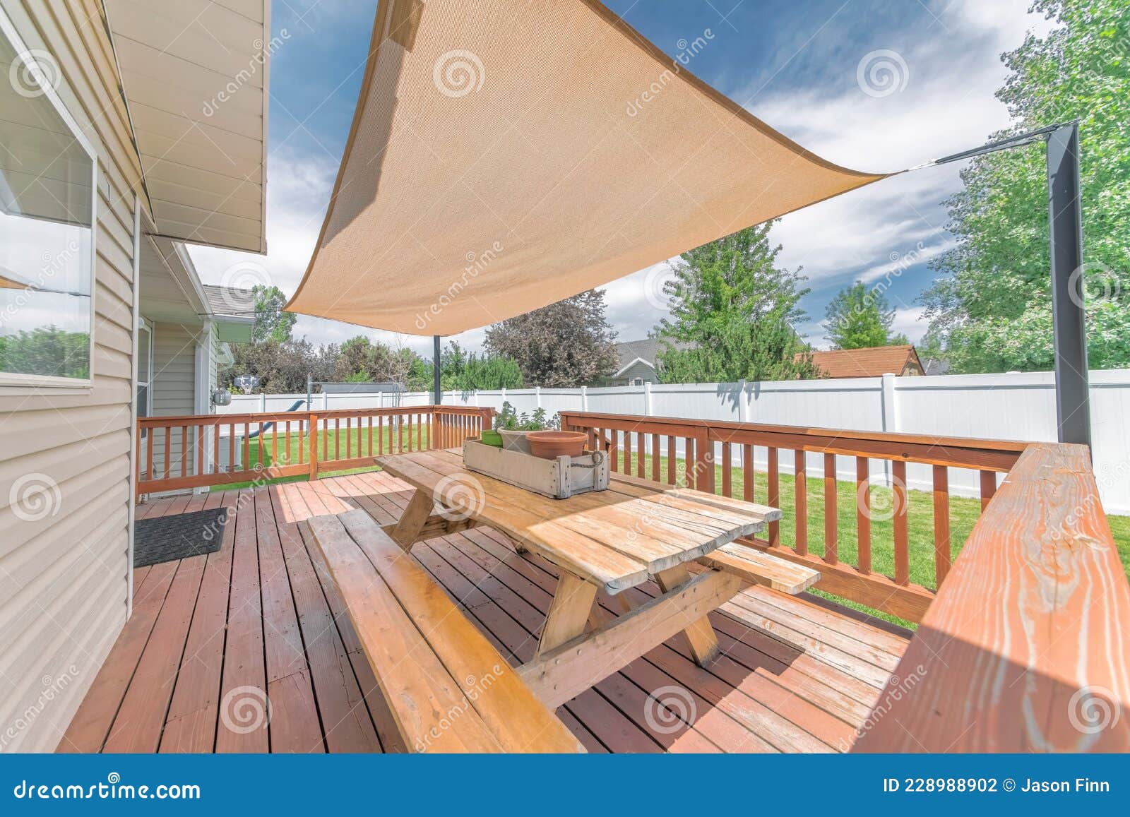 deck of a house with wooden chairs and table under a shade sail